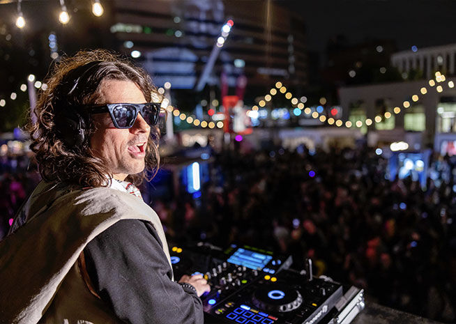 A DJ enraptures an evening crowd, his beats echoing through the cityscape.