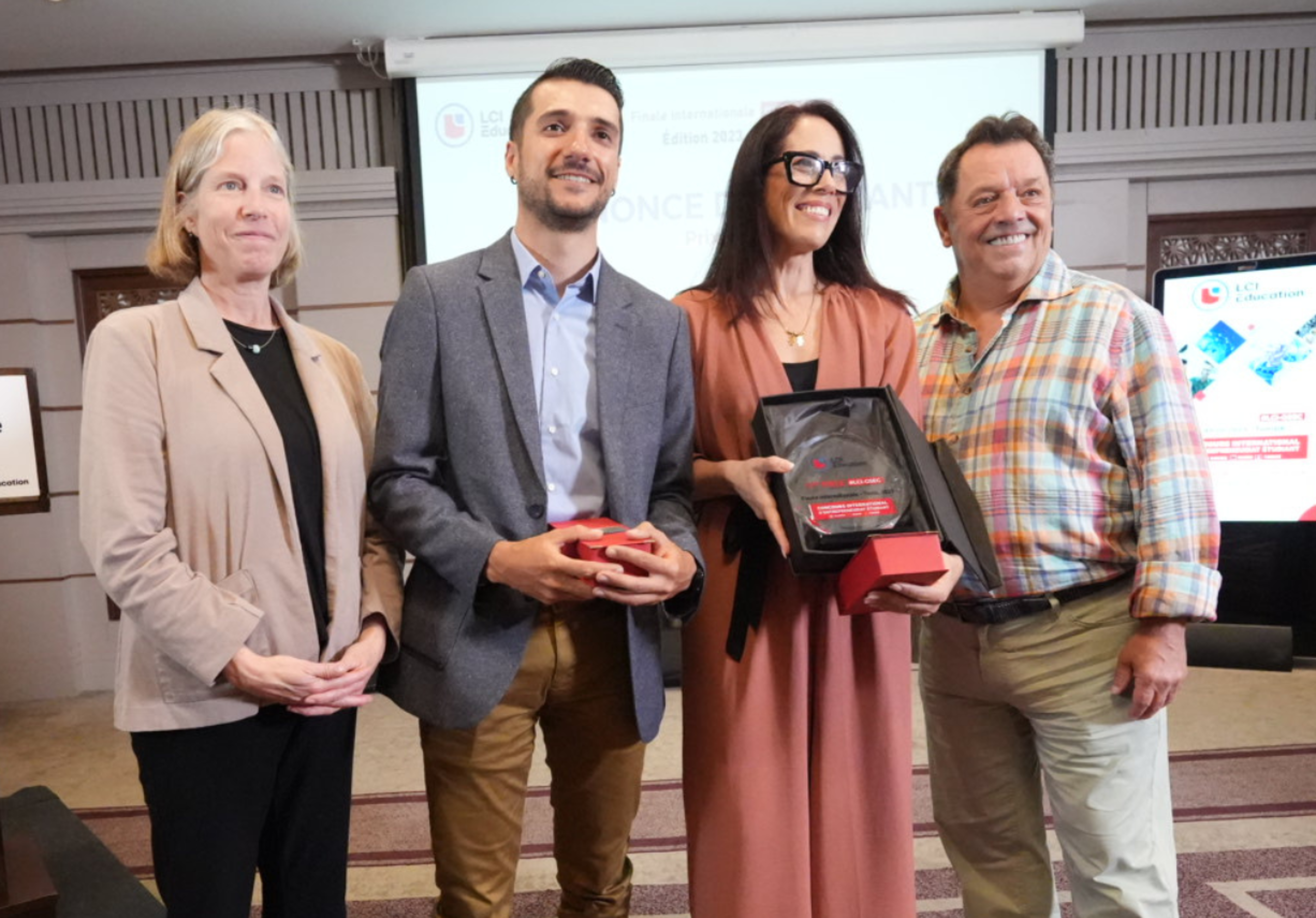 Group of professionals smiling, holding awards at an academic ceremony, with a presentation in the background.