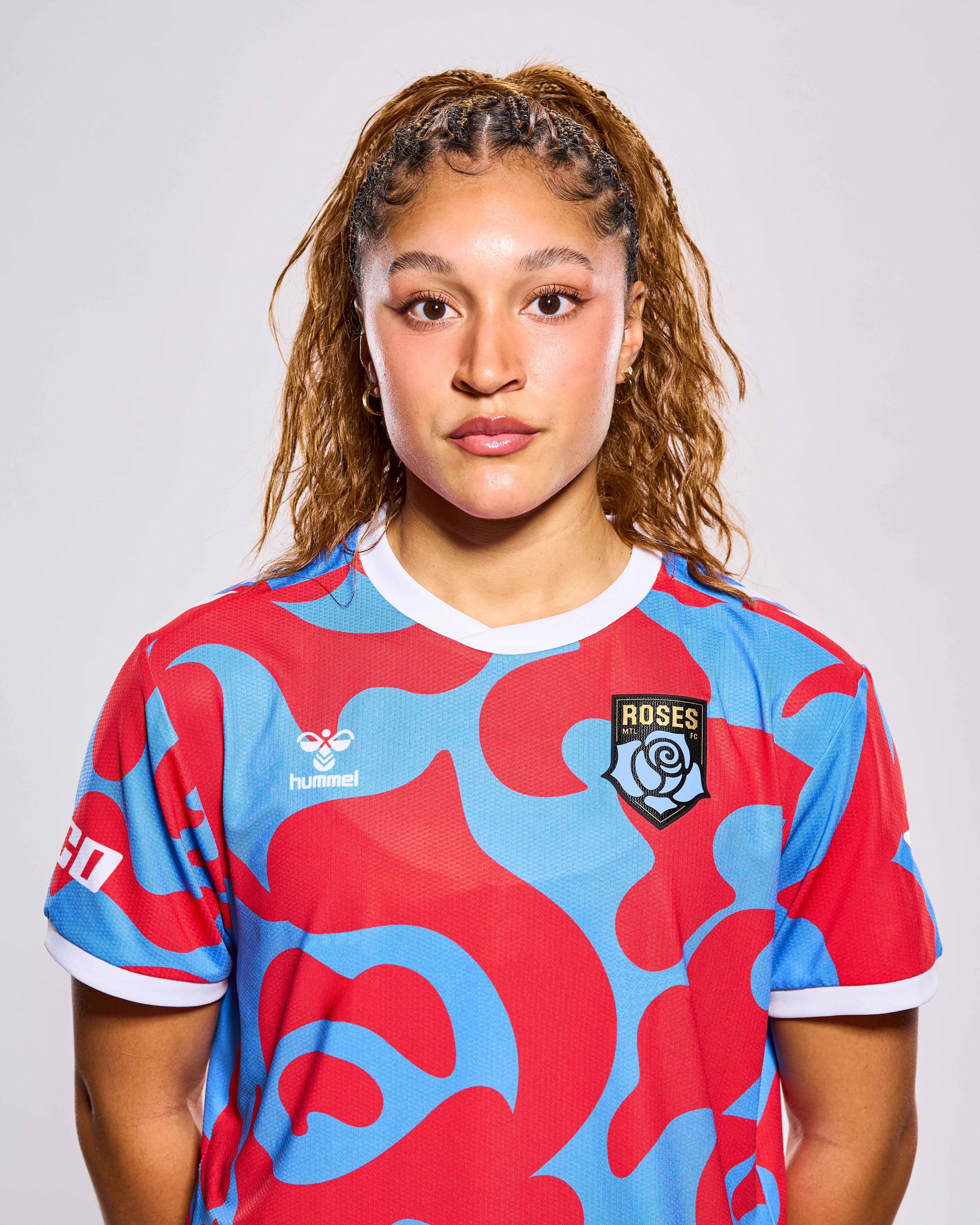 This is a photograph of a young woman with braided hair, wearing a red and blue soccer jersey with the "ROSES" logo on the sleeve.