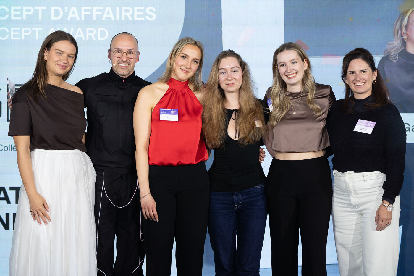 Six people, three women and three men, pose for a group photo at an event. They are all smiling at the camera.