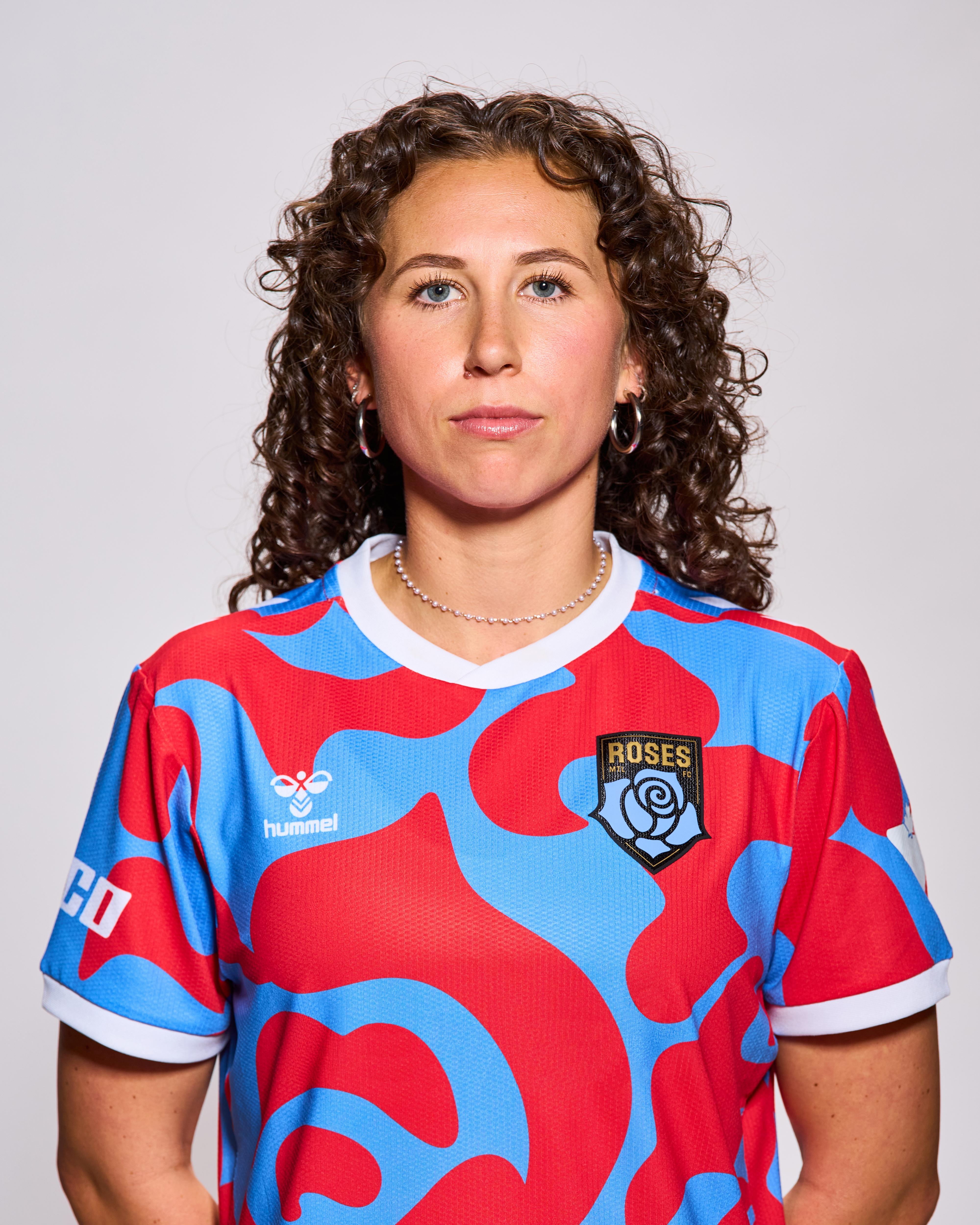A young woman with dark curly hair is wearing a blue and red sports jersey with the Roses logo on her left shoulder.
