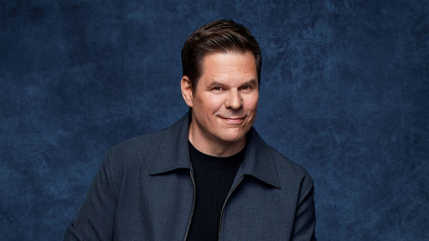 A smiling man in a blue jacket against a blue background.