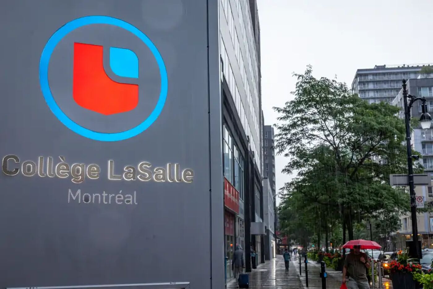 This is a close-up of a sign that reads 'Collège LaSalle Montréal'. It is a rainy day with people holding umbrellas walking down the street.