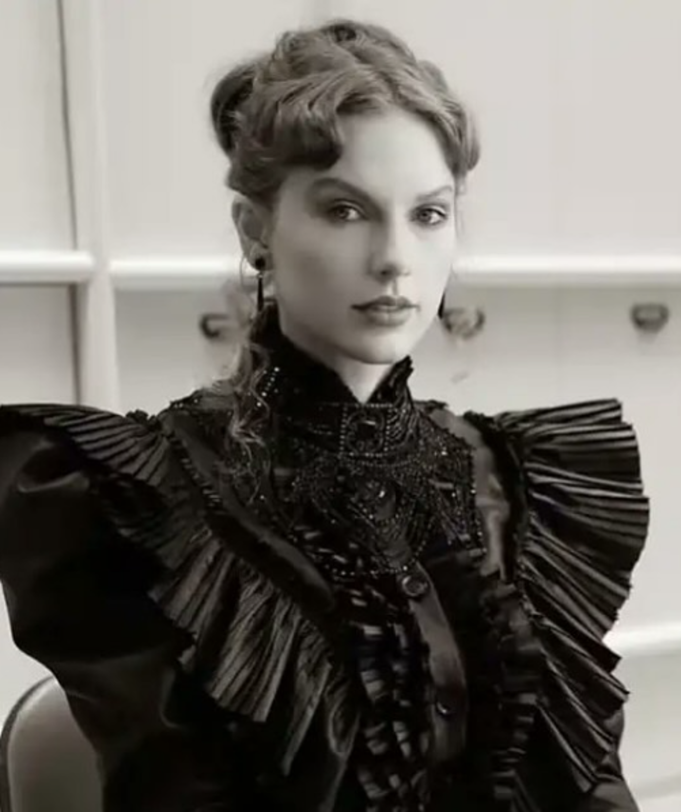 Close-up black and white shot of a woman with an elaborate hairstyle and Victorian-style black dress, her expression serious.