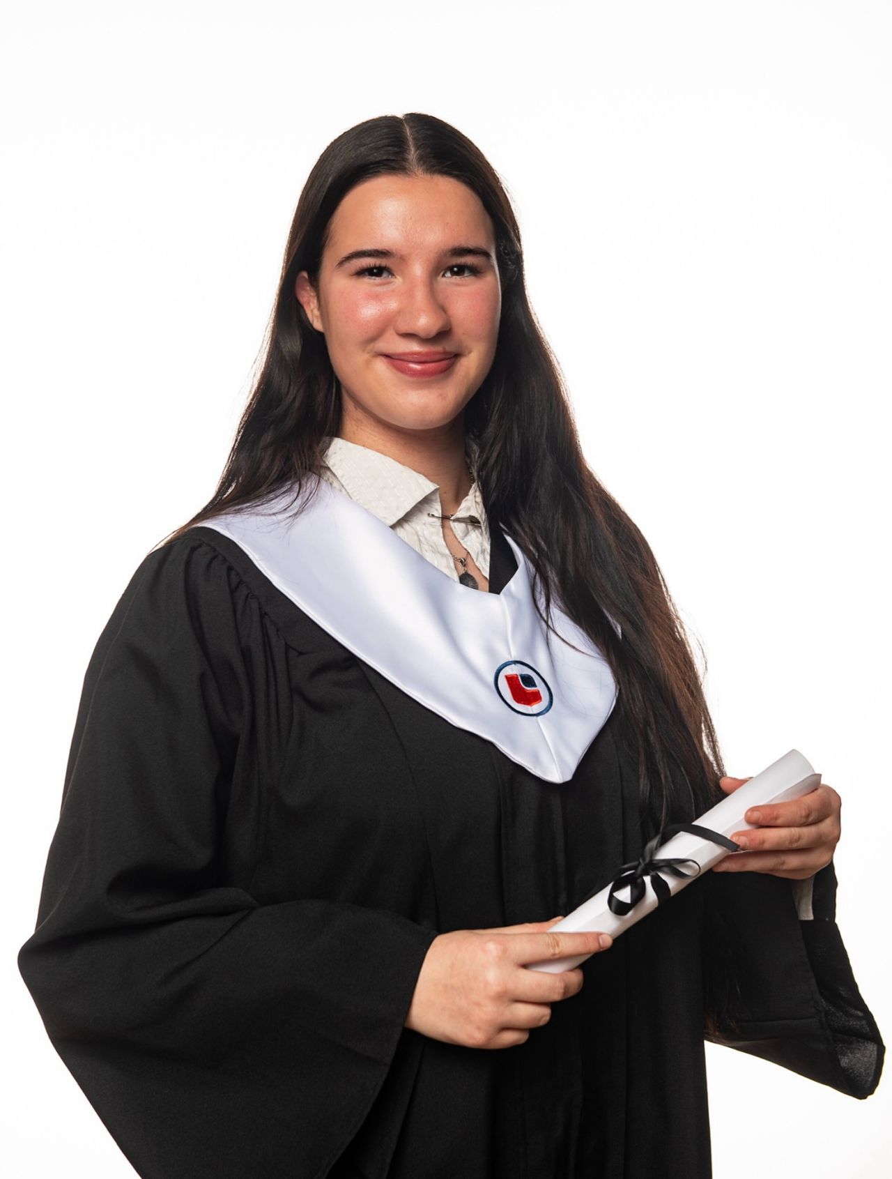 A young woman with long dark hair smiles while wearing a black graduation gown and holding a rolled-up diploma.