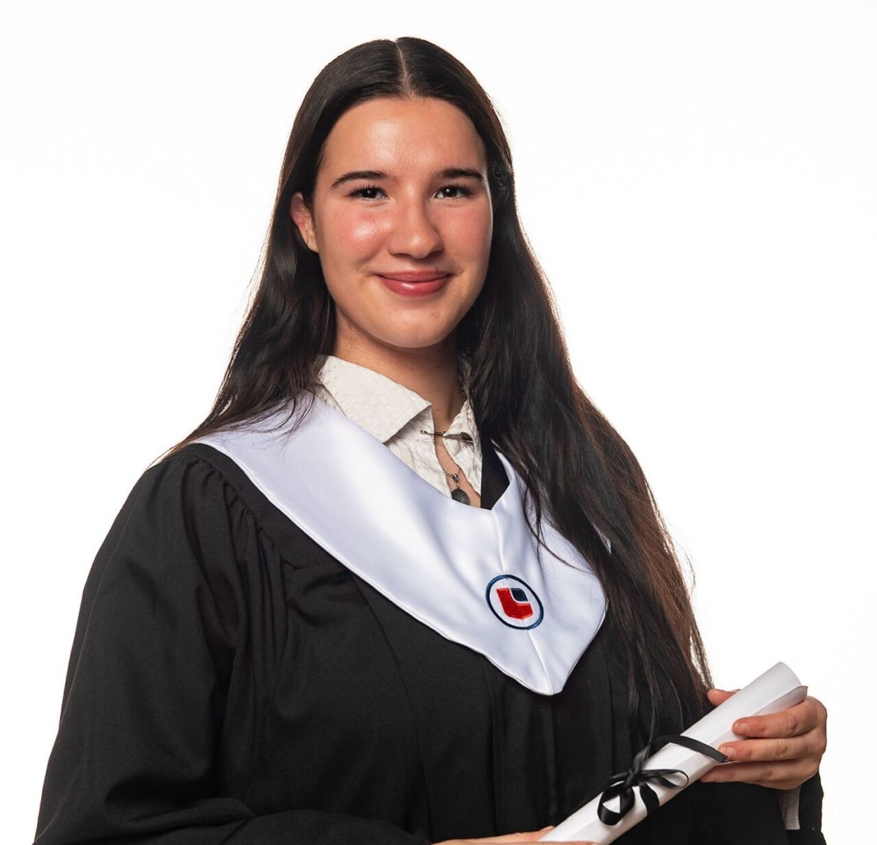 A young woman with long dark hair smiles while wearing a black graduation gown and holding a rolled-up diploma.