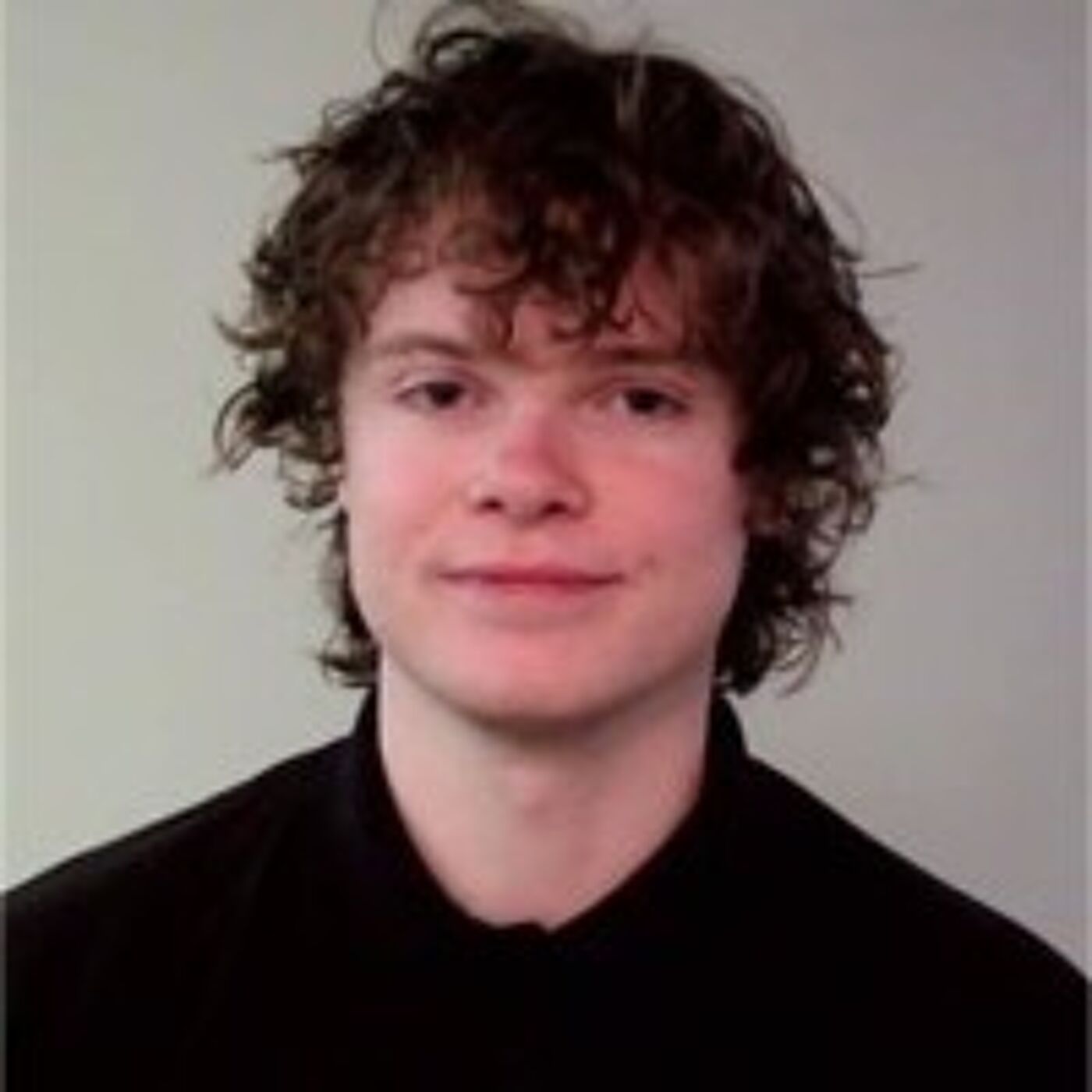 Close-up shot of a young man with curly brown hair wearing a black collared shirt.