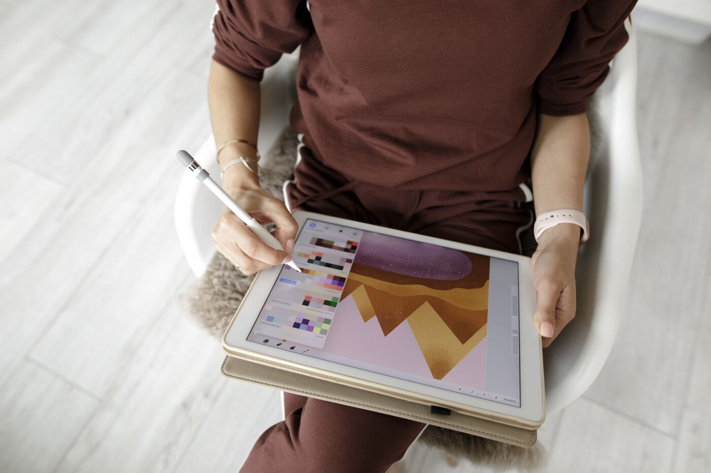  A person in a brown outfit sketches on a digital tablet with a stylus pen.