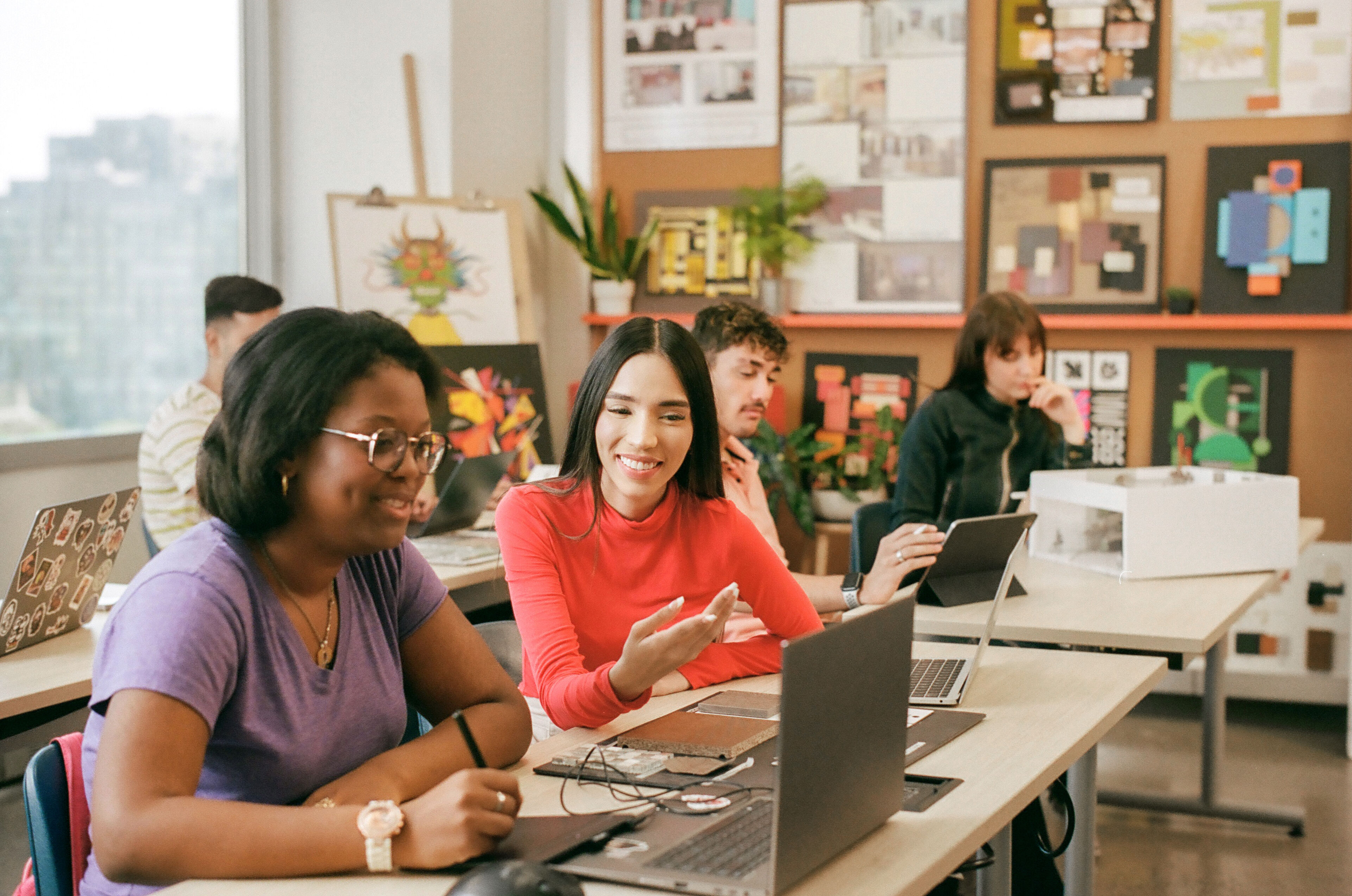 Adult students of various backgrounds engage with laptops and tablets in a bright classroom.