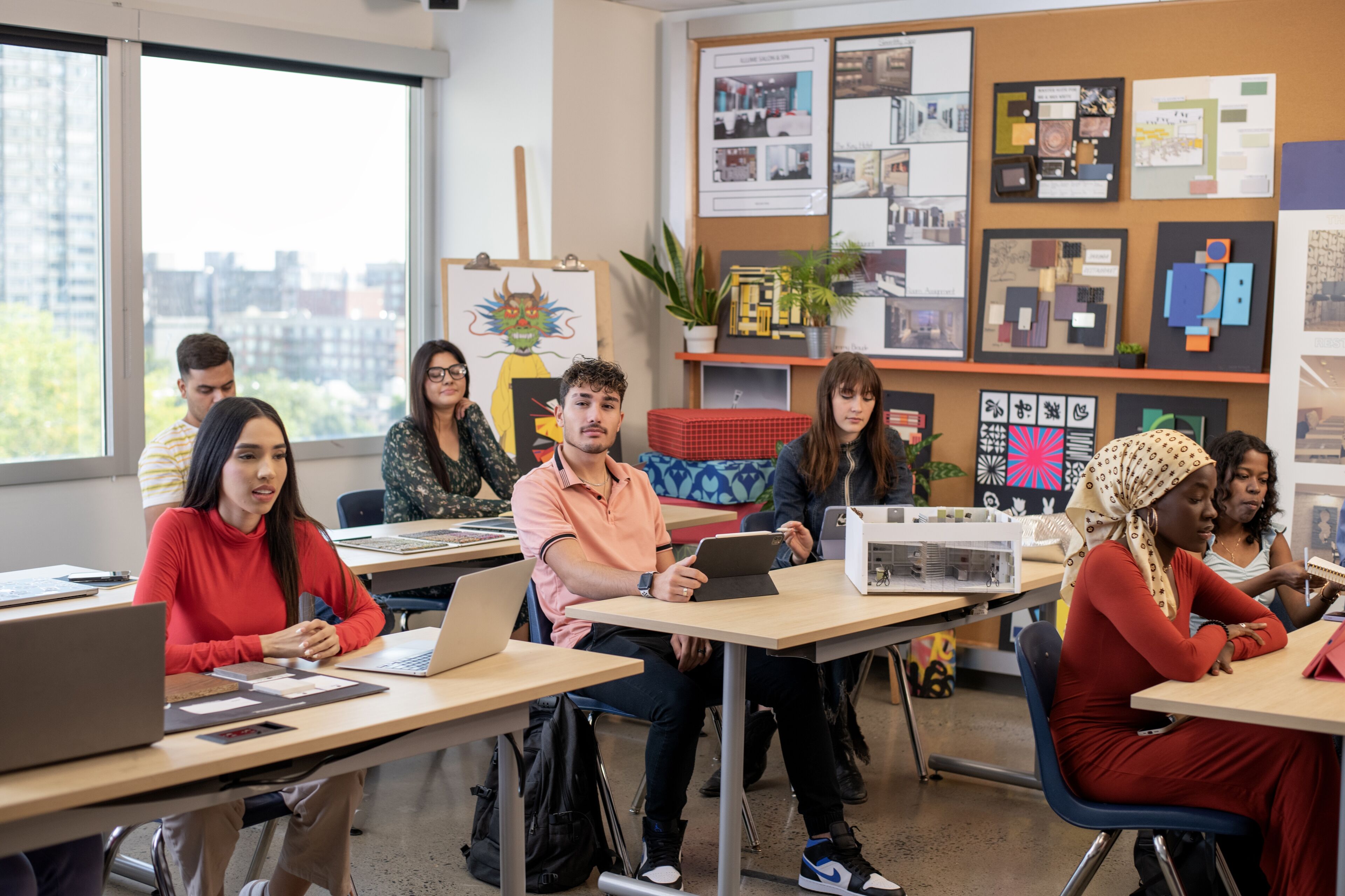 Adult students of various backgrounds engage with laptops and tablets in a bright classroom.