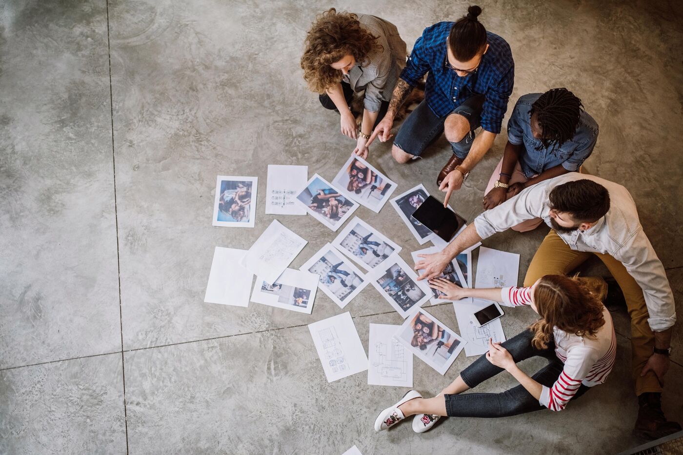 A group of people are sitting on the floor, reviewing images and documents, appearing to be in a brainstorming session or project meeting.