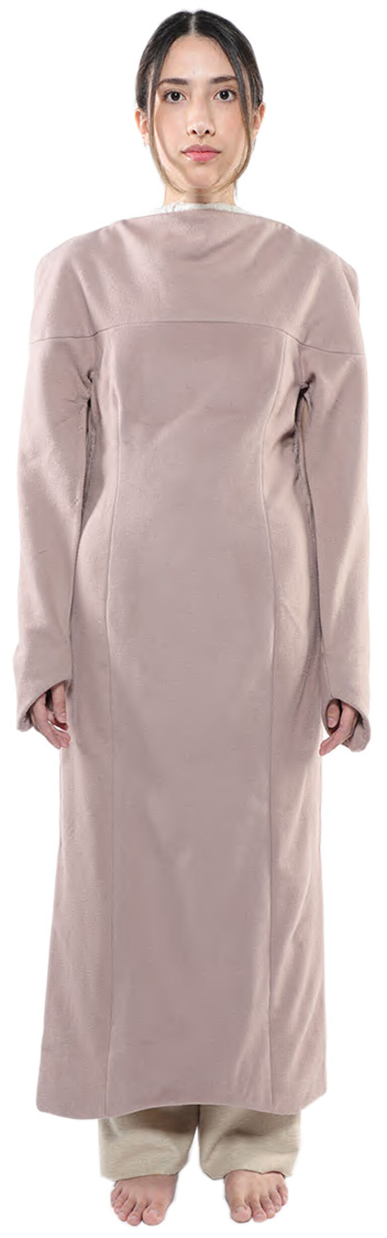 A woman with dark hair pulled back wears a long, light-brown, collared dress with long sleeves and stands with her feet together.
