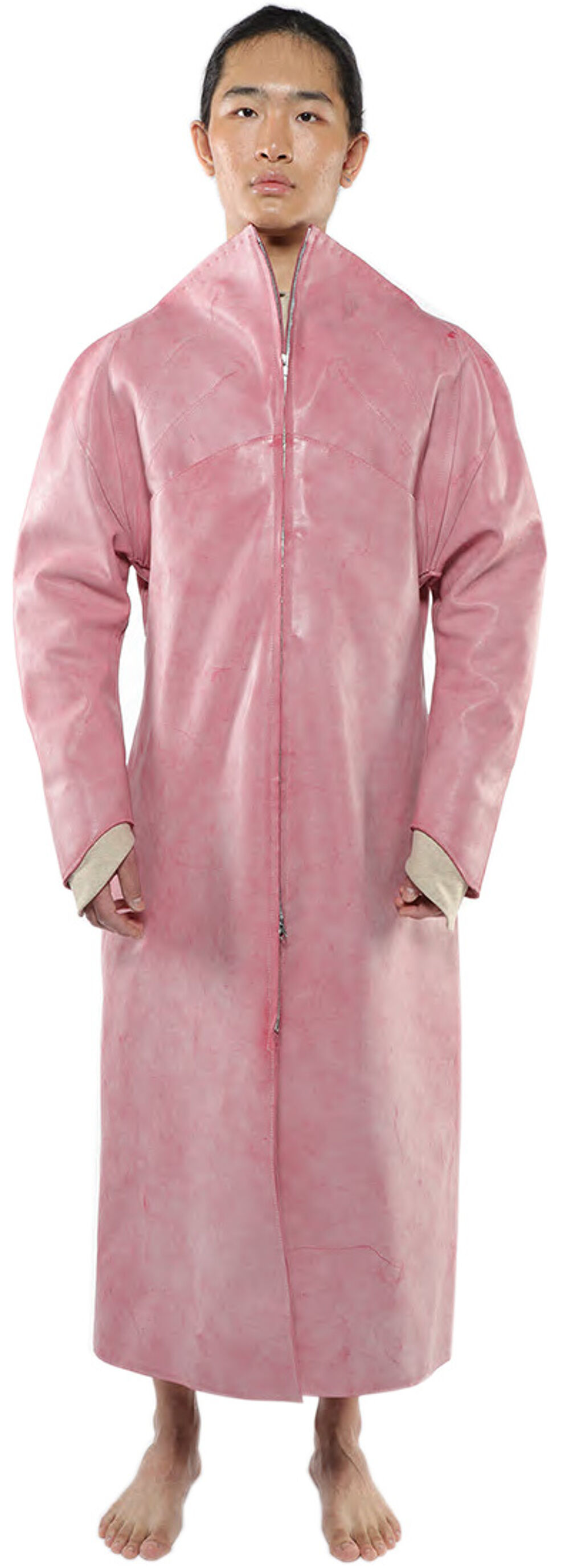 A person with tan skin and dark hair is standing and wearing a long, pink coat that zips up the front.