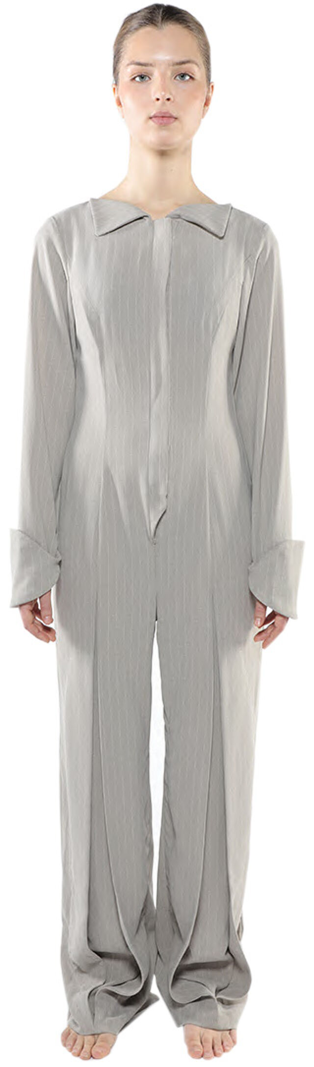 A woman stands facing forward, wearing a light gray, long-sleeved jumpsuit with a collared neckline.