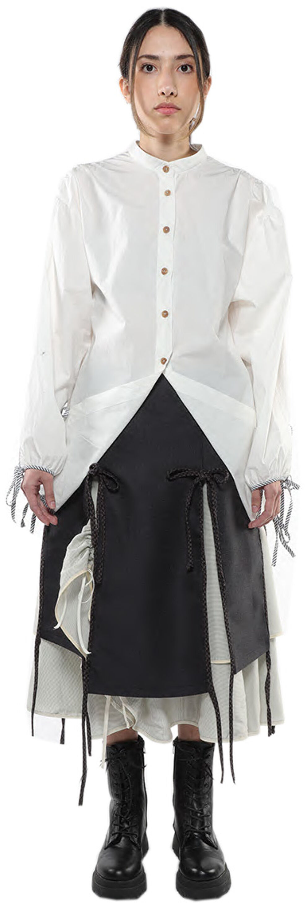 A woman with dark hair pulled back wears a long-sleeved white shirt over a dark gray skirt and black lace-up boots.