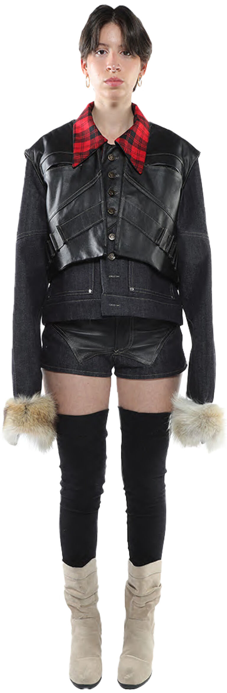 A young woman with short dark hair models a black leather vest over a denim jacket, paired with black leather shorts, black tights, and beige boots, accessorized with red and black plaid fabric at the collar and fur wrist cuffs.