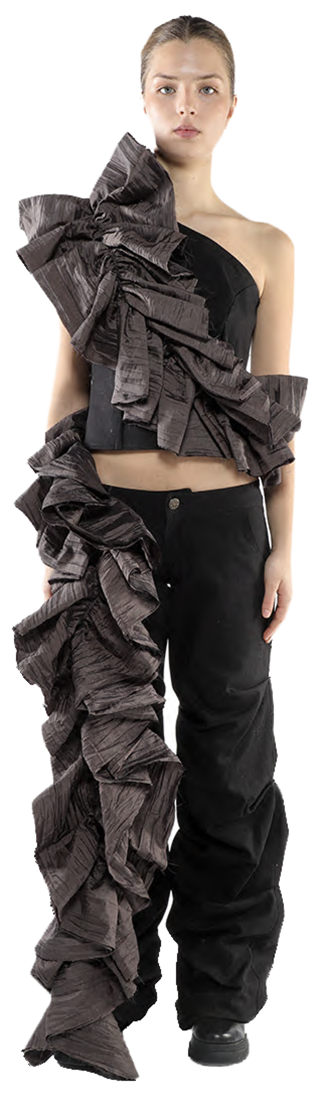 A young woman with light skin and dark hair is modeling an avant-garde outfit consisting of a dark gray asymmetrical top with voluminous ruffles and black pants.
