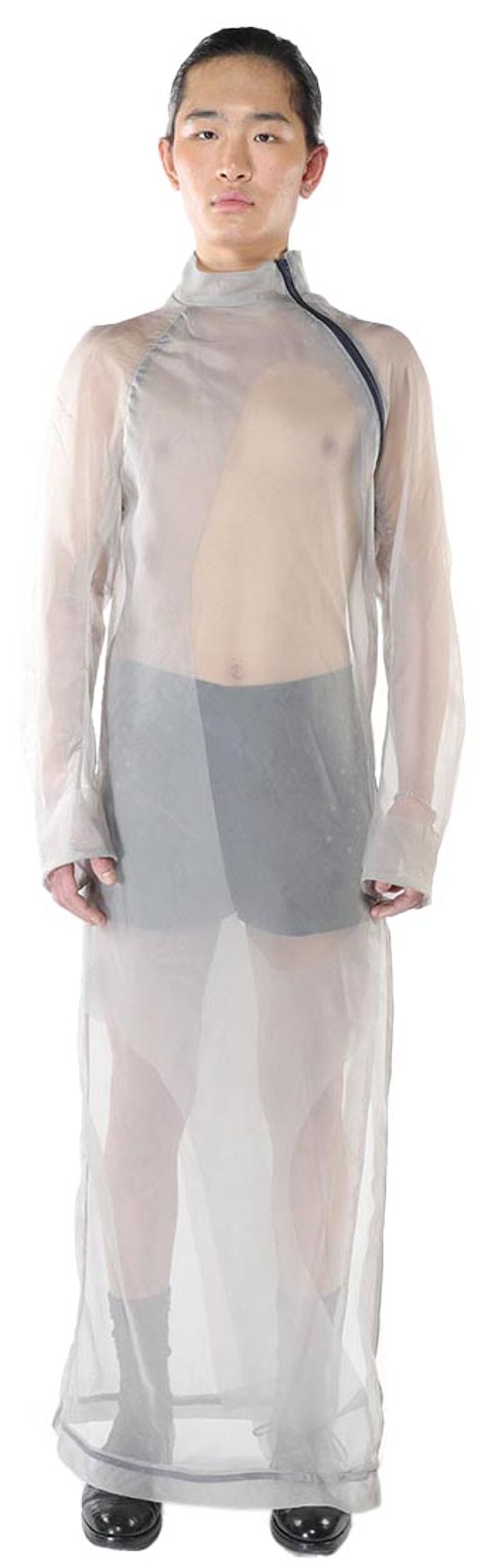 A person with dark hair is wearing a sheer, long-sleeved, light gray dress with dark gray shorts underneath.