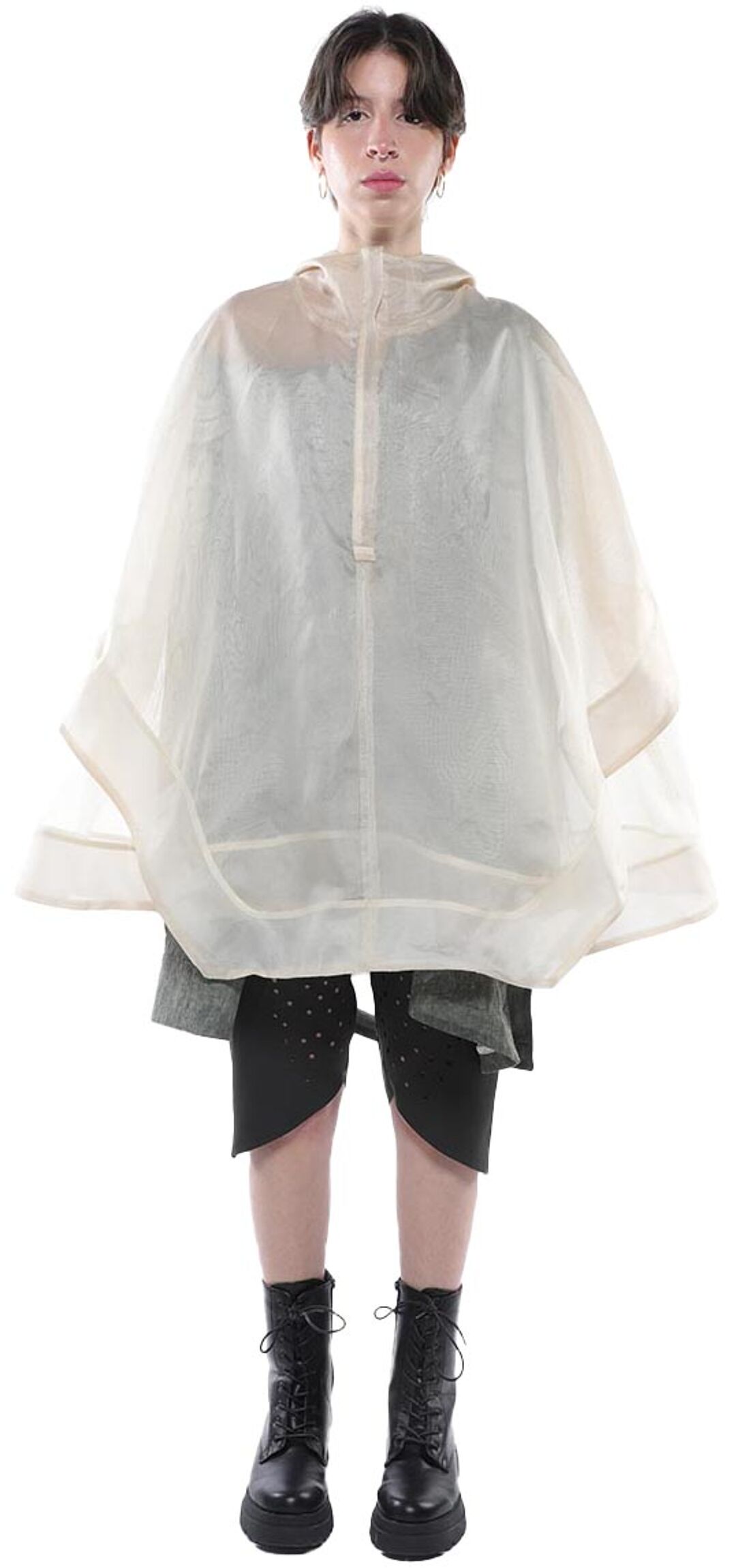 A person wearing a beige poncho, dark-colored shorts, and black combat boots stands against a white background.
