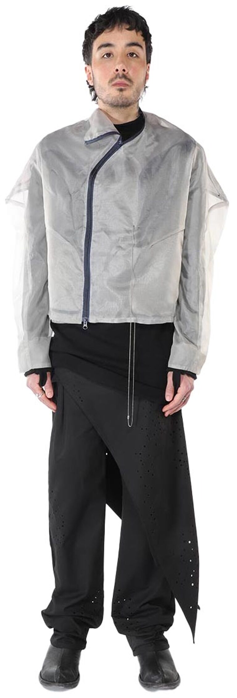 A male model is shown wearing a light gray, asymmetrical jacket over a black, asymmetrical skirt and pants, with dark shoes.
