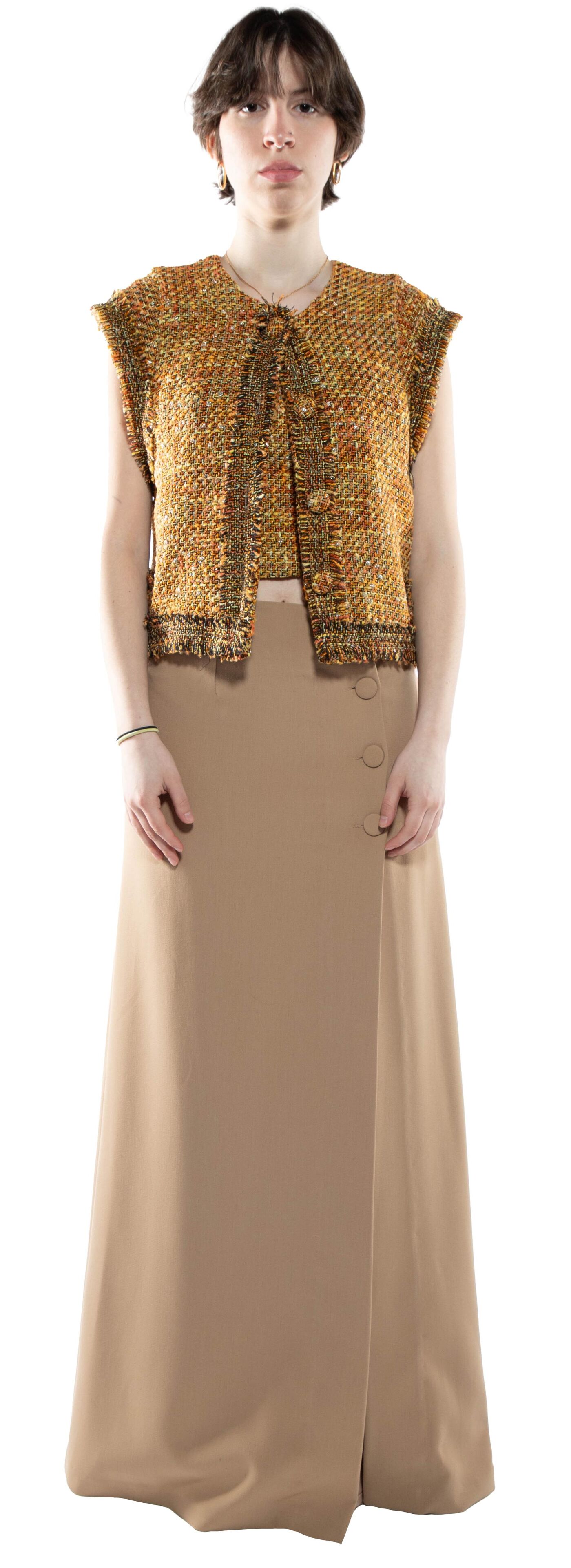 A woman with short brown hair wears a gold tweed vest over a beige midi skirt with buttons down the front.