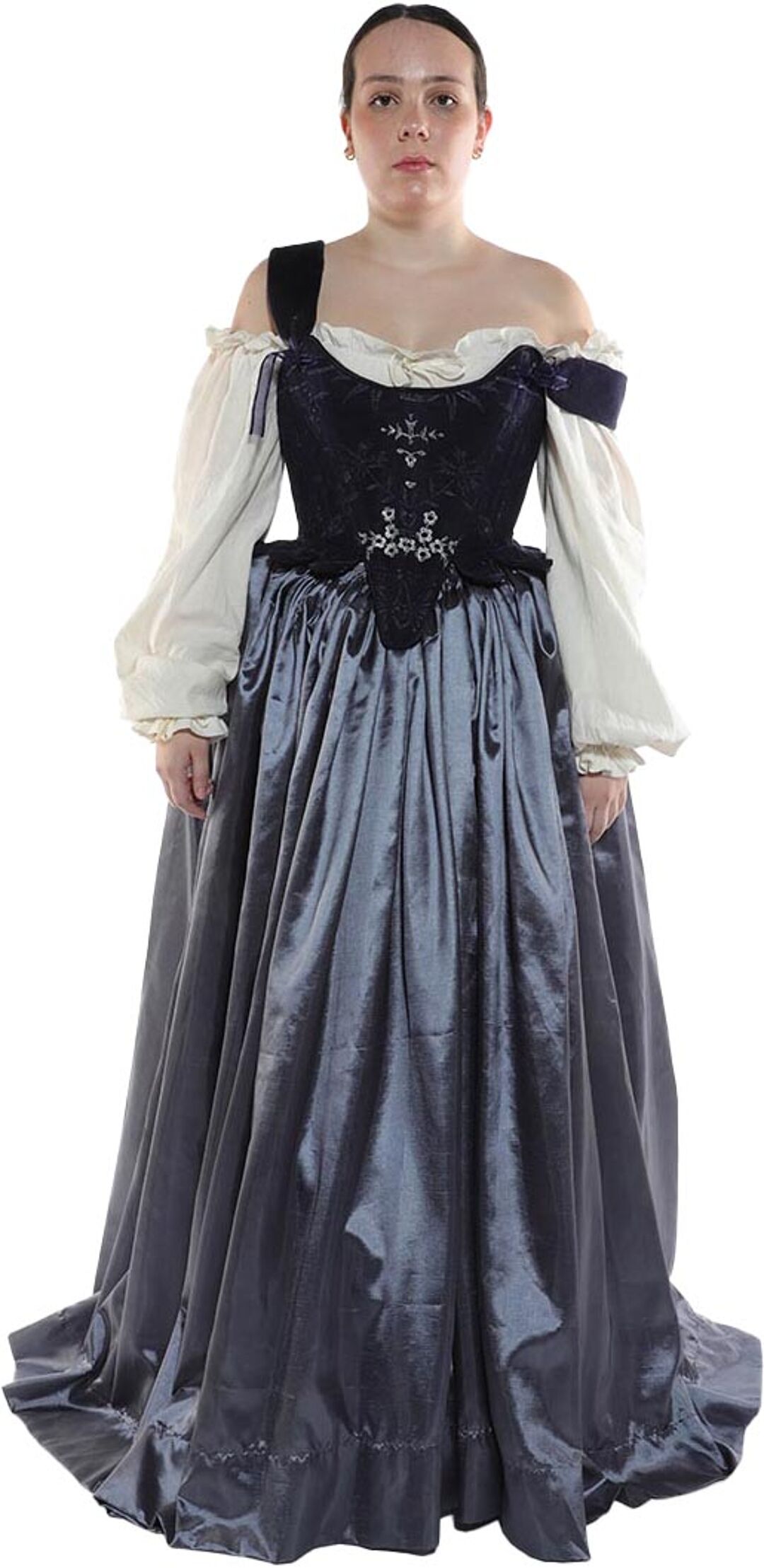 A woman with light skin and dark hair wears a long, dark gray gown with a darker, embroidered bodice and off-white, puffed sleeves.