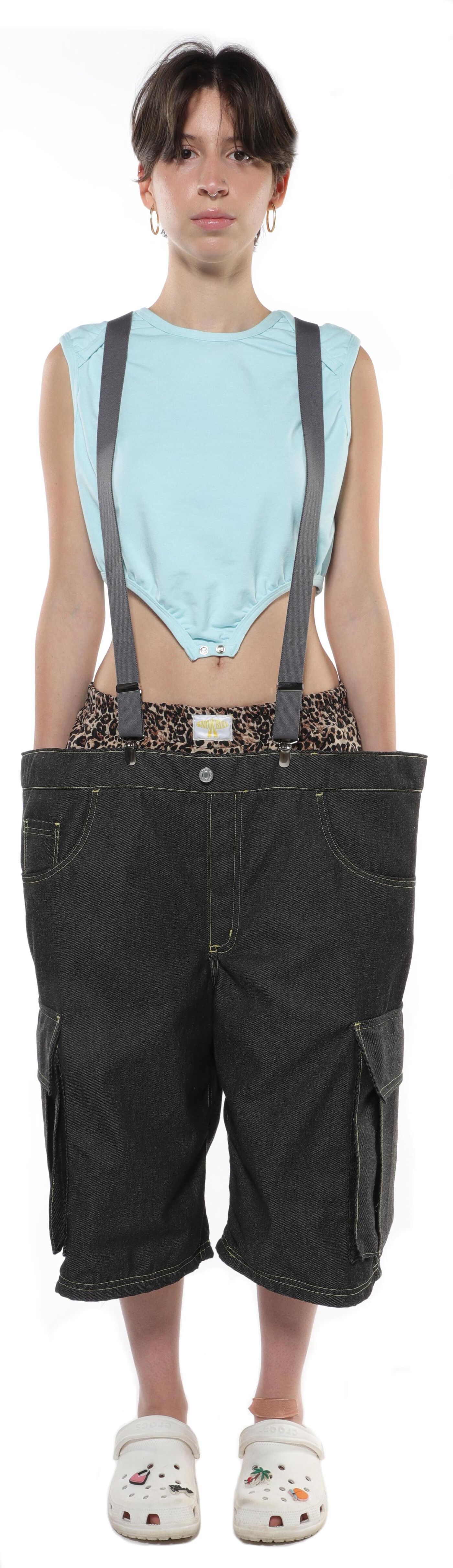 A young person with short brown hair wears a light blue cropped top, leopard print underwear, dark cargo shorts, and white clogs.