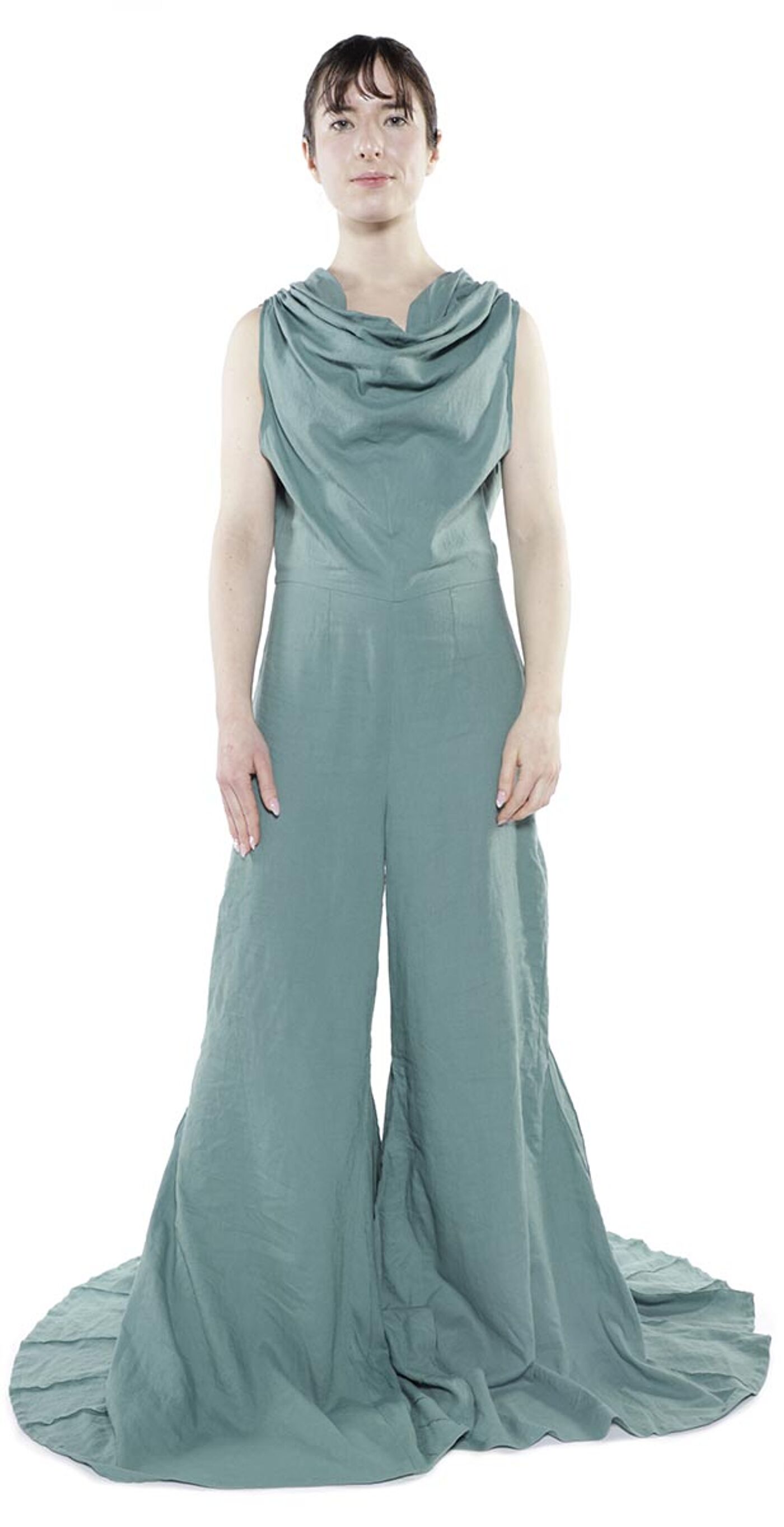 A woman with dark hair pulled back wears a flowing, sea-foam green jumpsuit with a cowl neck and wide legs that pool on the floor.