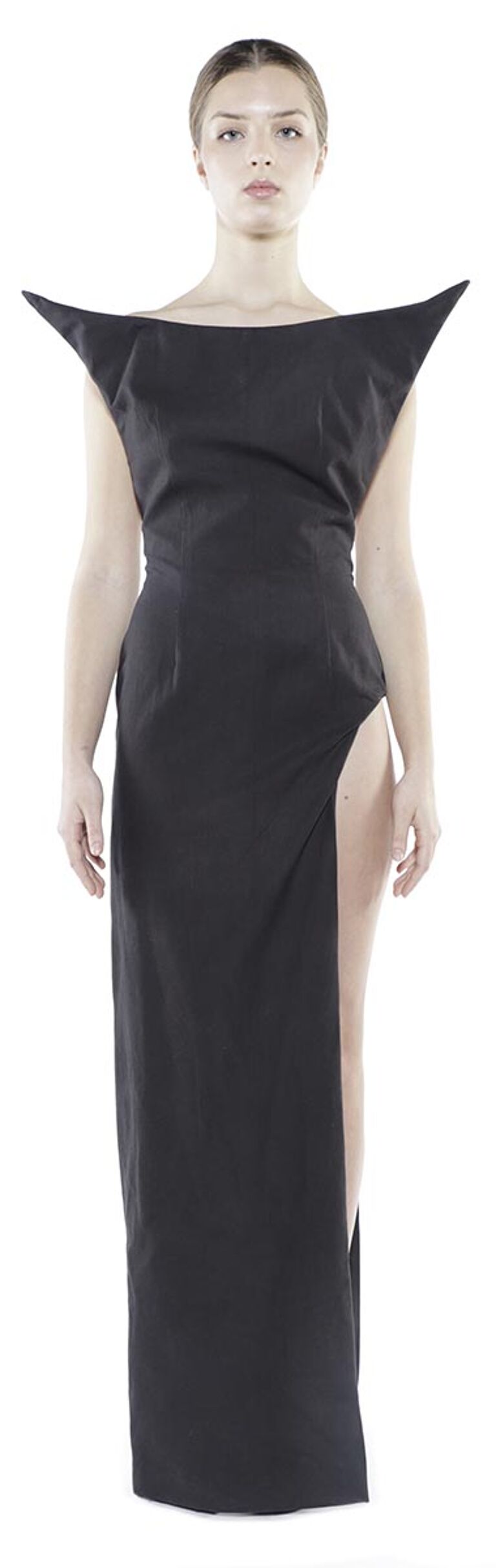 A slender woman with light skin and dark hair is modeling a long, black, sleeveless dress with a high, angular neckline and a thigh-high slit on one side.