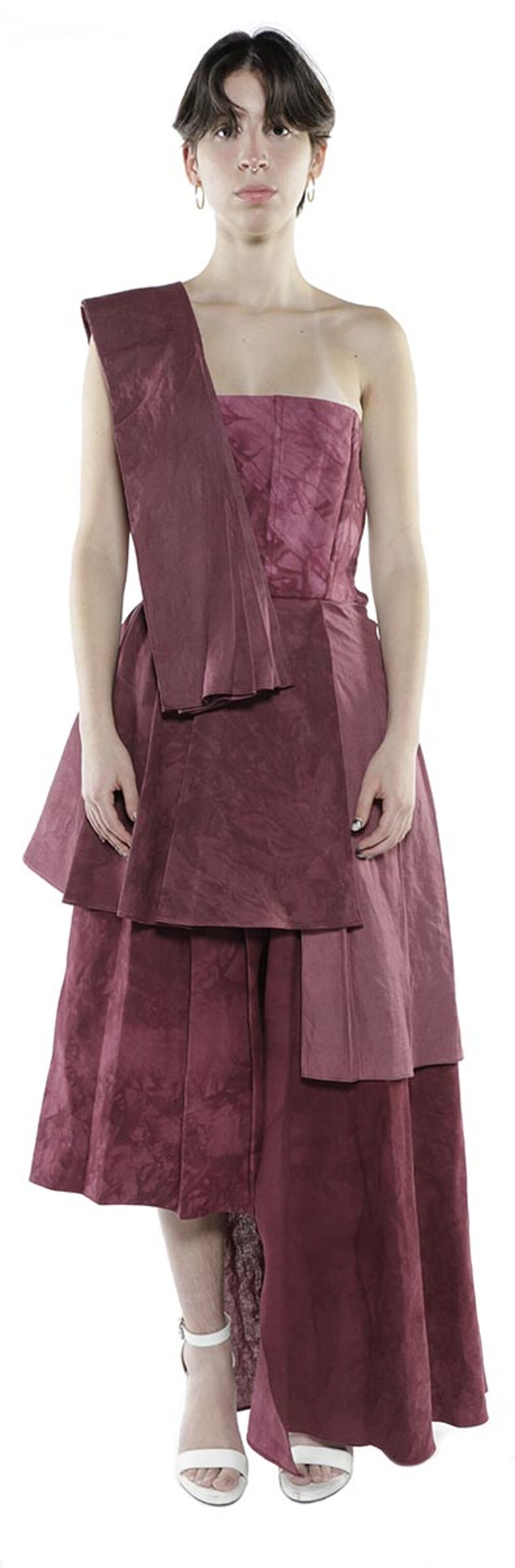 A woman with short brown hair wears a layered, asymmetrical maroon dress and white heels.
