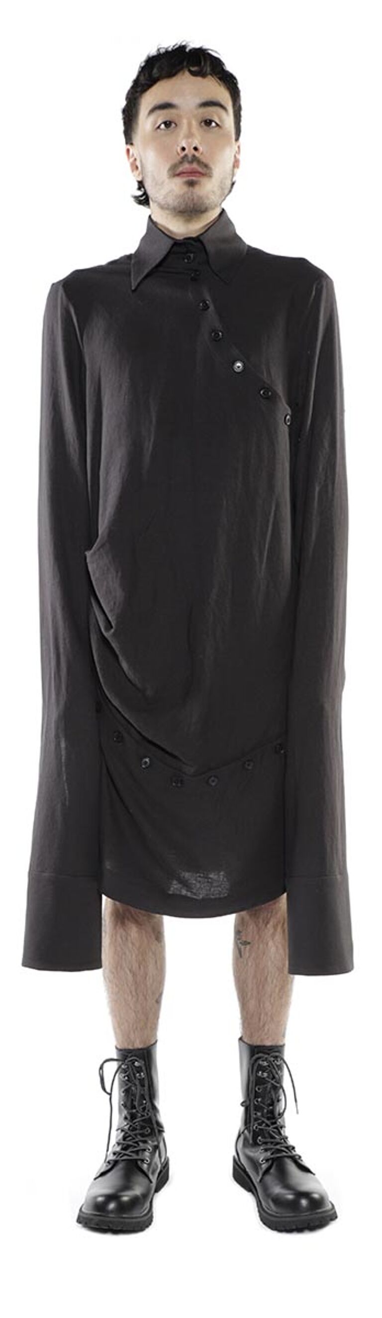 A person with dark hair and skin is modeling a long-sleeved, dark-colored shirt dress that falls to their mid-thighs, paired with black combat boots.