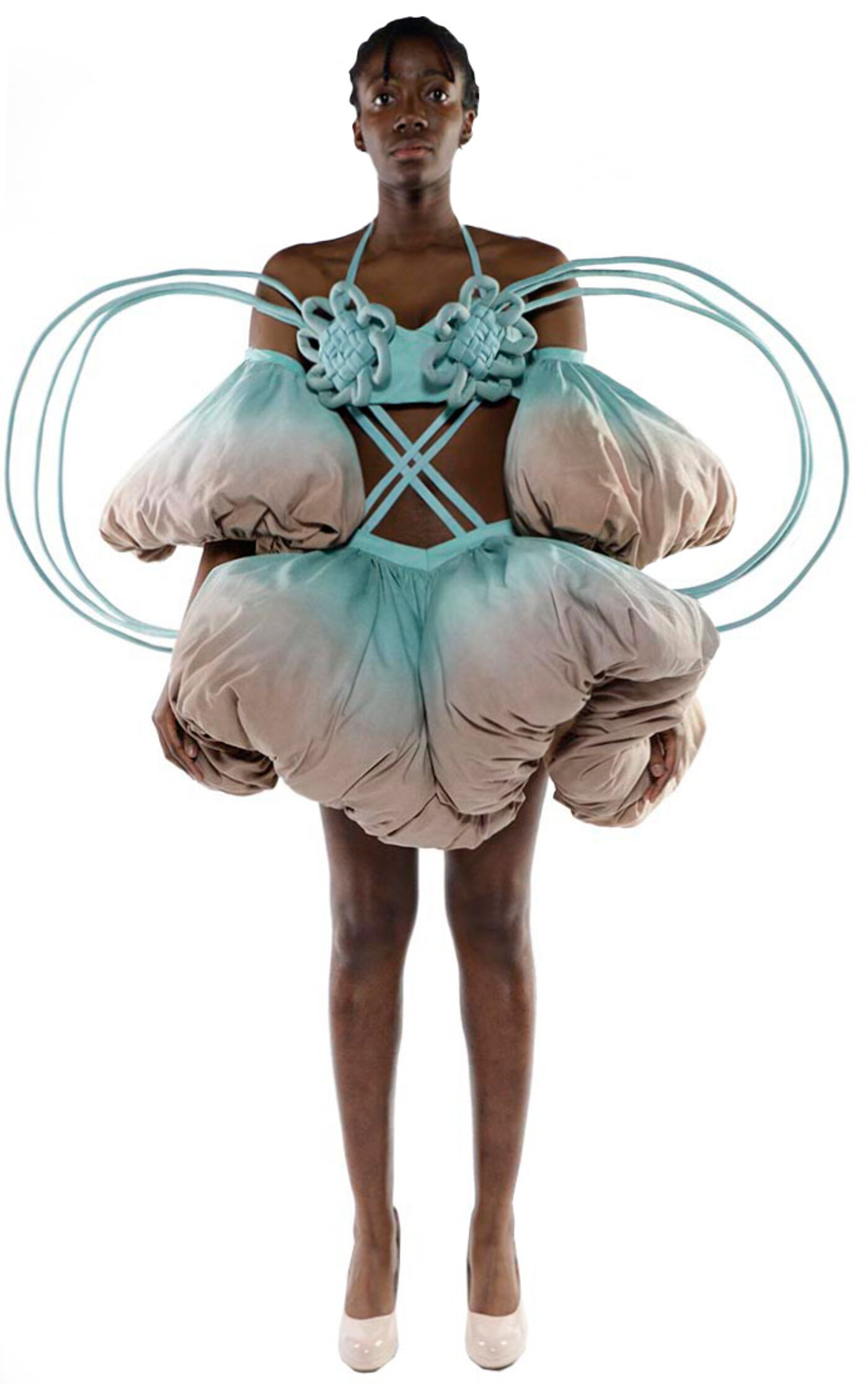 A dark-skinned model wears a unique, puffy, light-blue and beige dress with circular accents and light-pink heels.