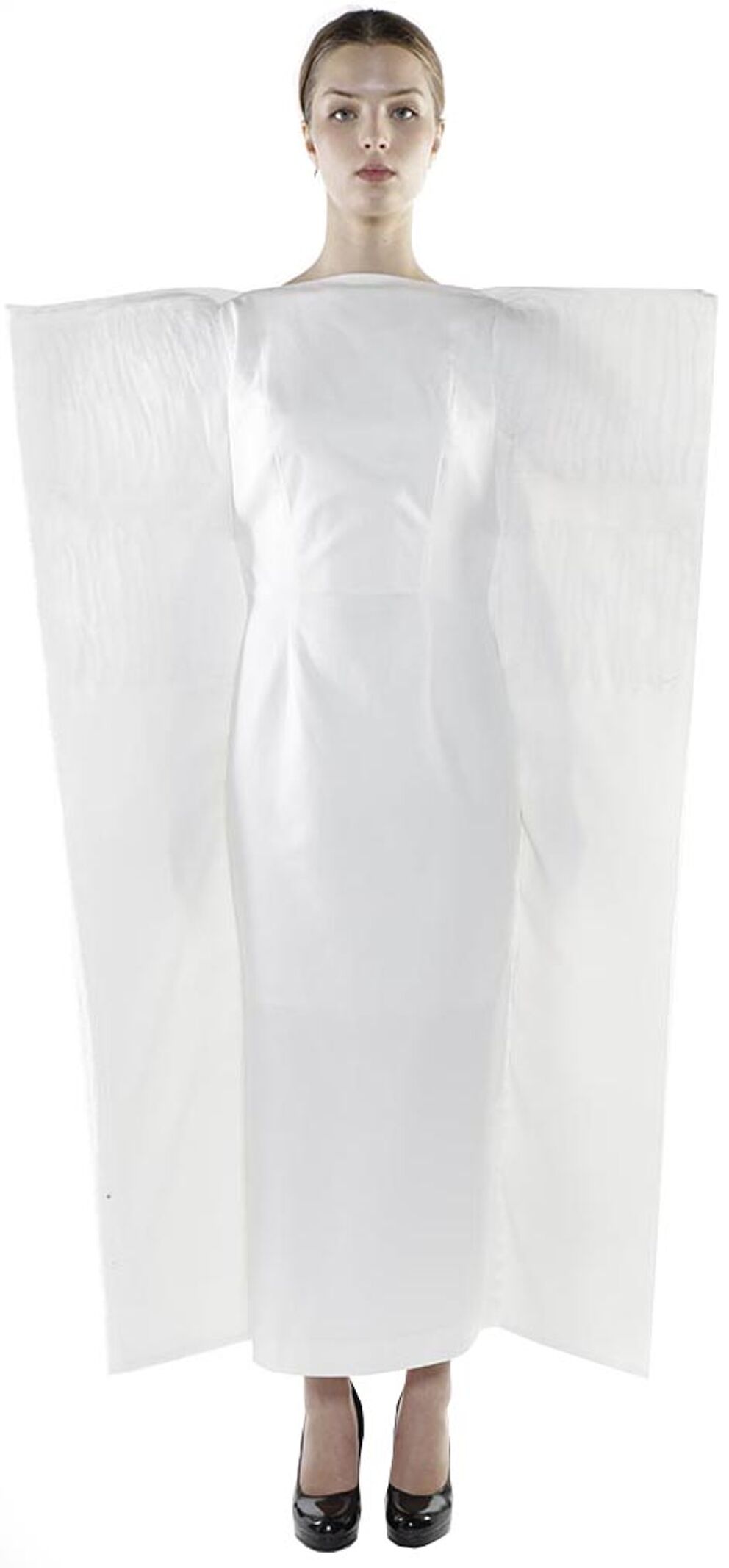 A woman in a long white dress with oversized, sheer white fabric draped over her shoulders stands against a white background.