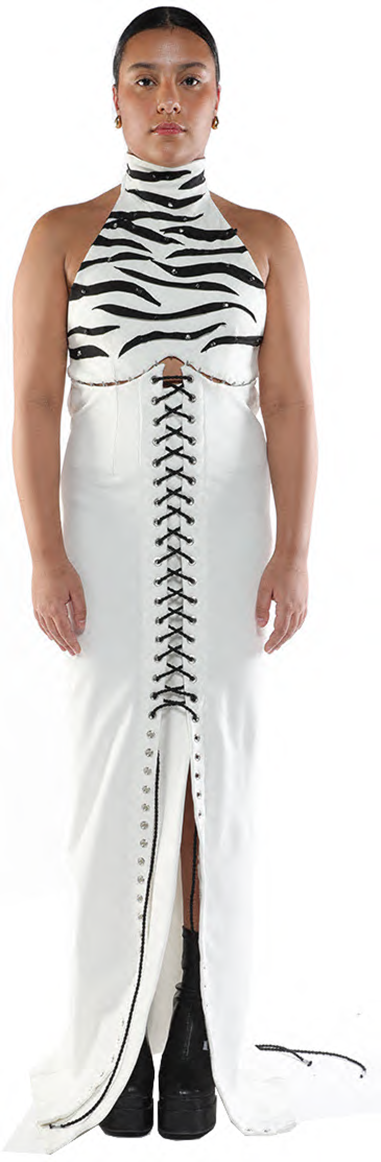 A woman with tan skin and dark hair wears a white maxi skirt with a black and white zebra-striped halter top and black combat boots.