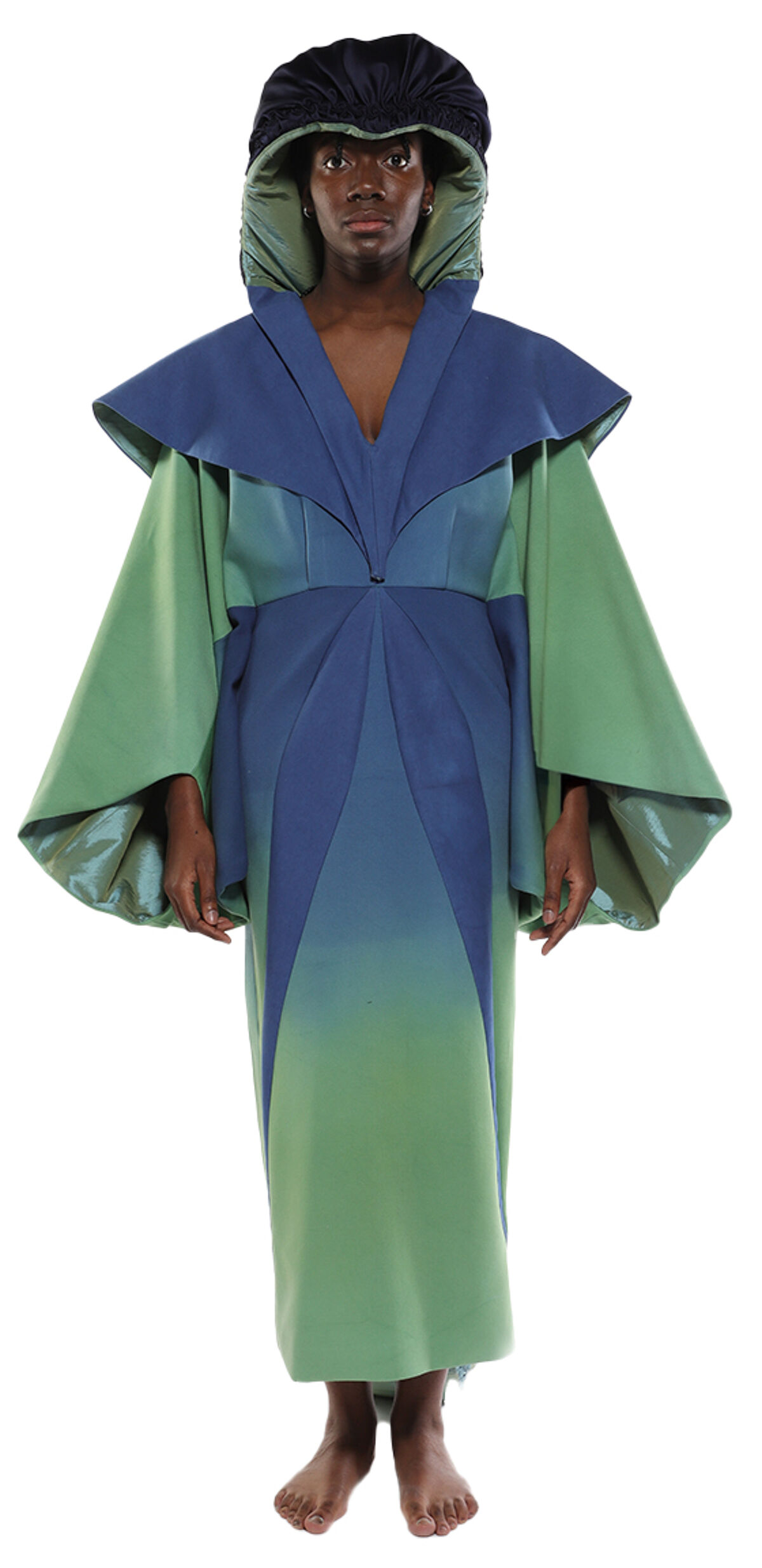 A person wearing a long, ombre-colored robe with wide sleeves and a matching hooded headpiece stands against a white background.