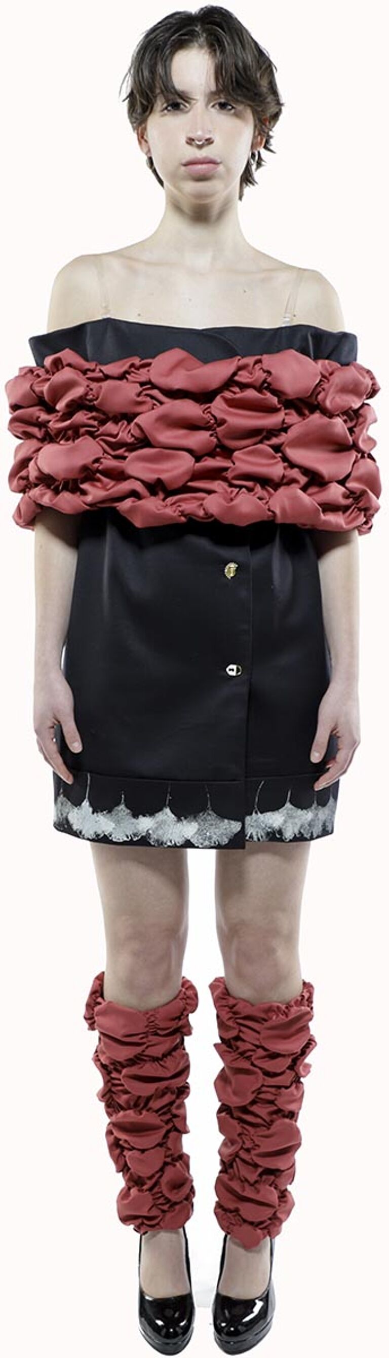 A young woman with short brown hair is modeling a black mini dress with a ruffled, coral-colored off-the-shoulder top and matching leg warmers, paired with black shoes.