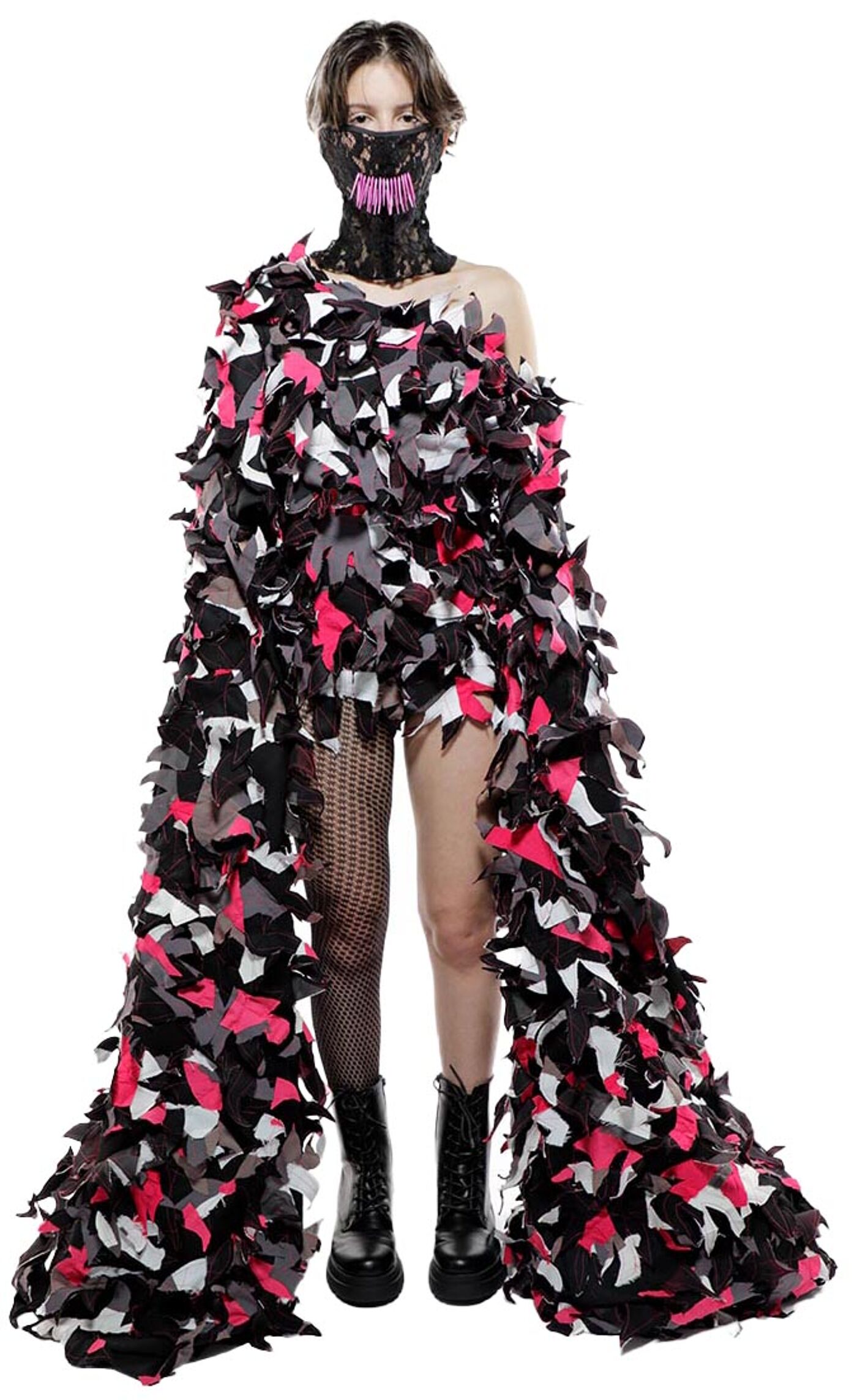 A model wears a black and pink camouflage-patterned dress and black lace mask with pink accents, accessorized with black combat boots and fishnet stockings.