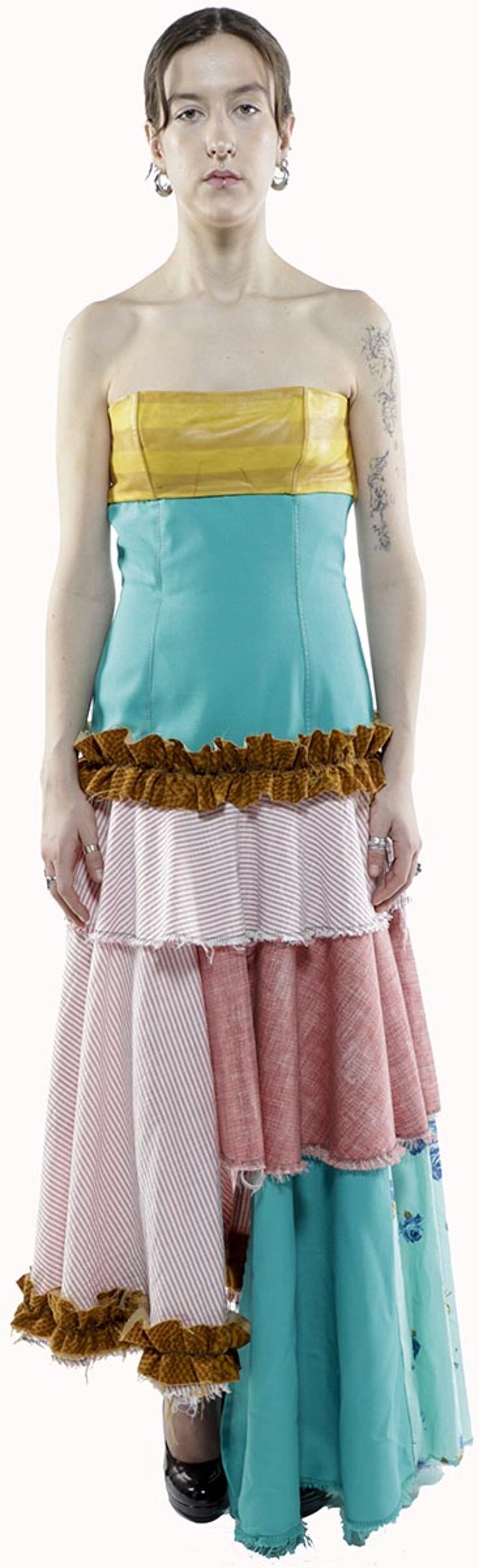 A woman with short brown hair wears a strapless, layered dress with a yellow bodice, teal midsection, and a multi-colored, tiered skirt of pink, white, and teal.