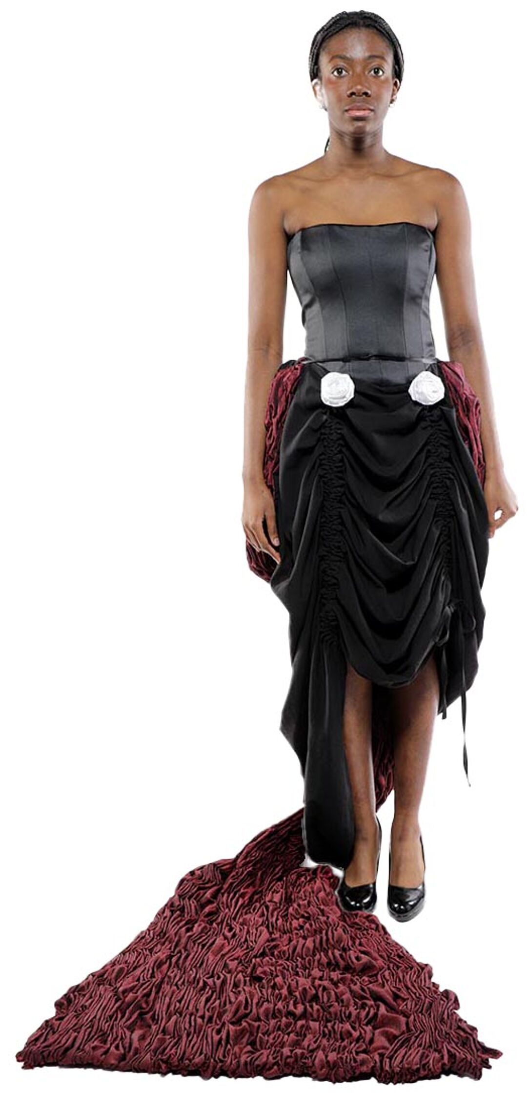 A dark-skinned woman in a black corset and a long, burgundy, pleated skirt stands against a white background.