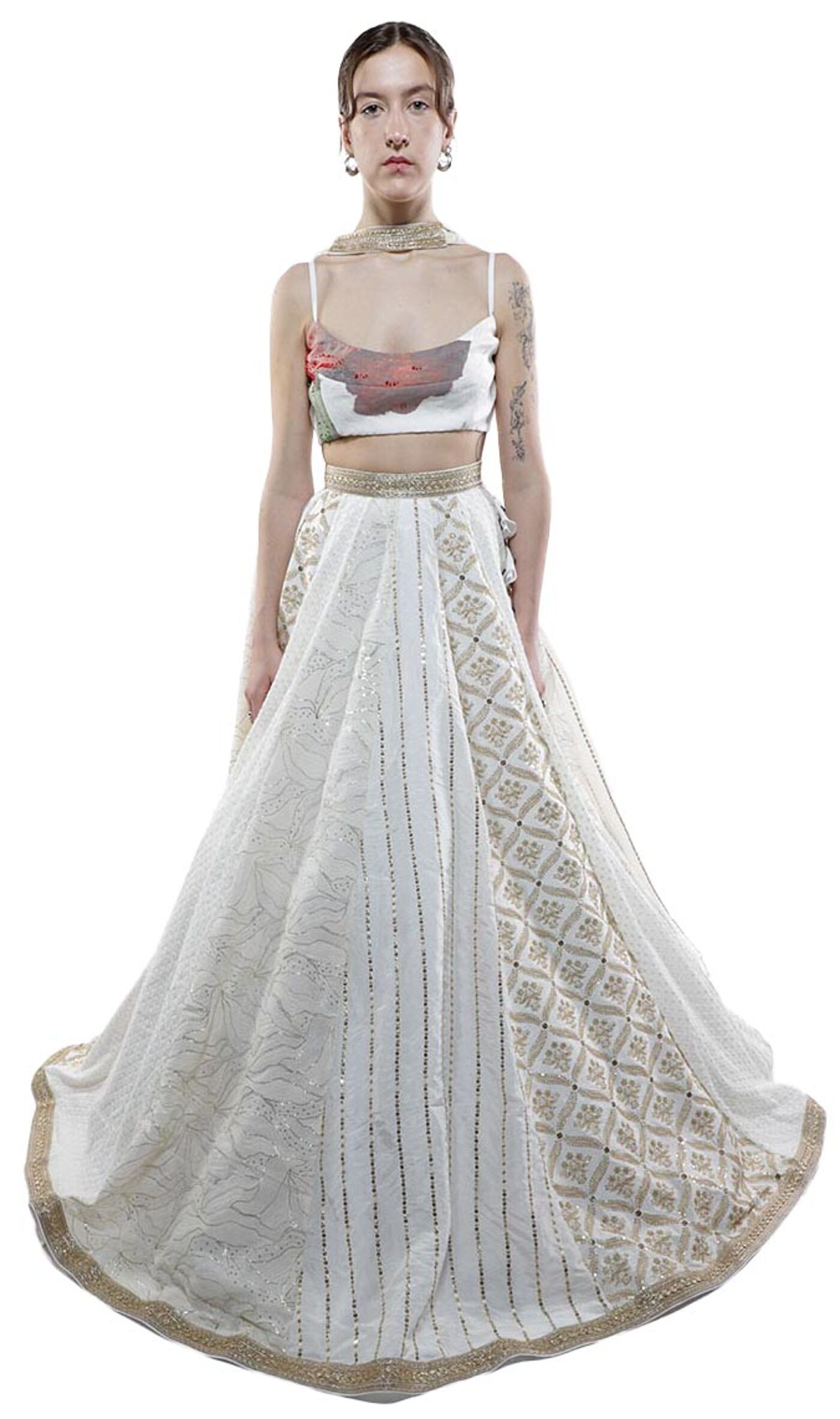 A woman with light skin and dark hair models a long, off-white, embroidered lehenga with a fitted, printed crop top.