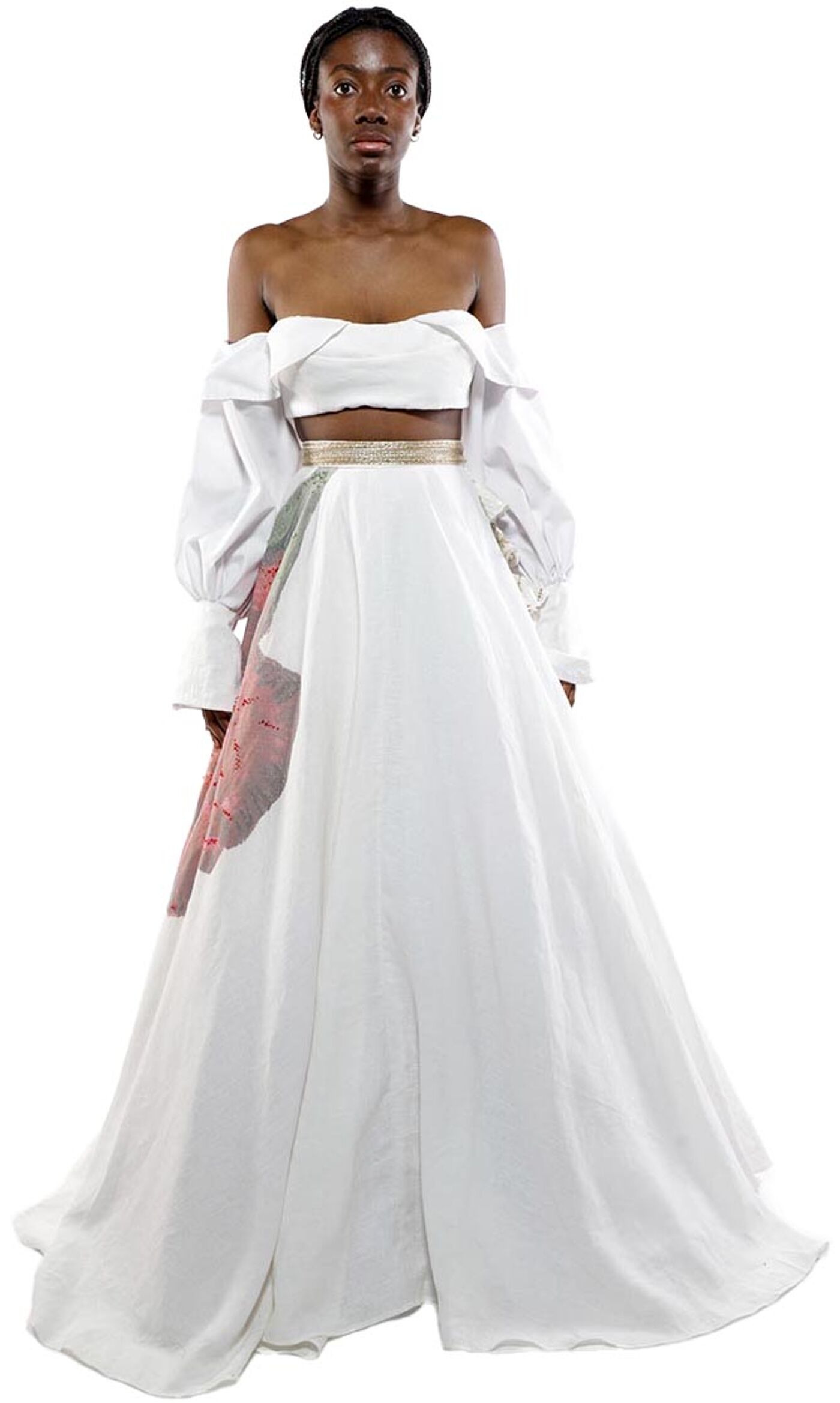 A dark-skinned woman with dark hair pulled back stands facing forward in a white off-the-shoulder long-sleeve top and matching long skirt with a partially visible patterned overlay.