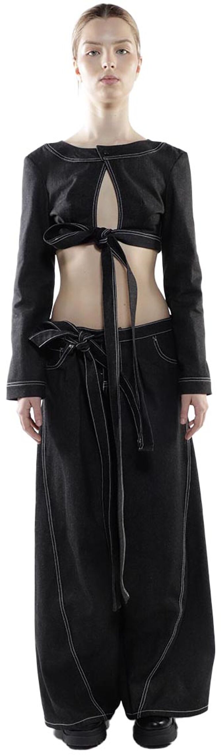 A woman is modeling a black long-sleeved crop top and wide-leg pants, both featuring white stitching detail and a tie at the waist.