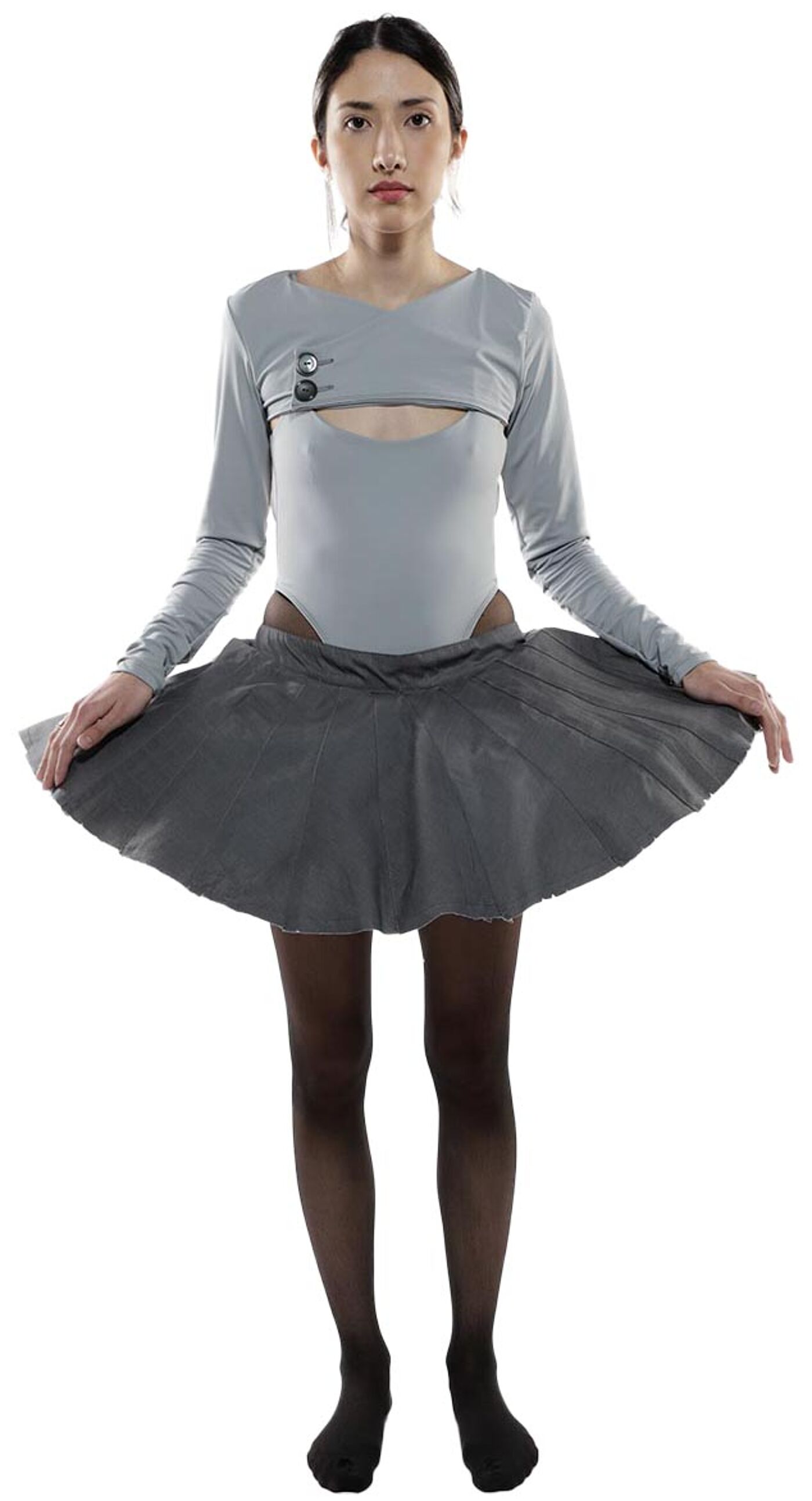 A young woman with dark hair and fair skin wears a light gray, long-sleeved leotard and a dark gray tutu.
