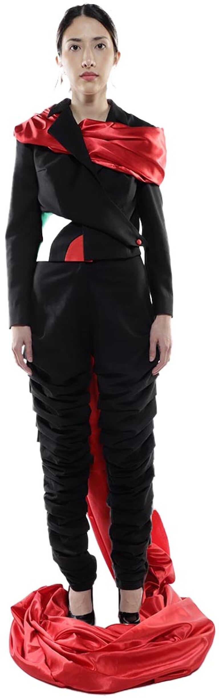 A woman in a black jumpsuit with a red draped fabric detail stands on a red fabric pool.