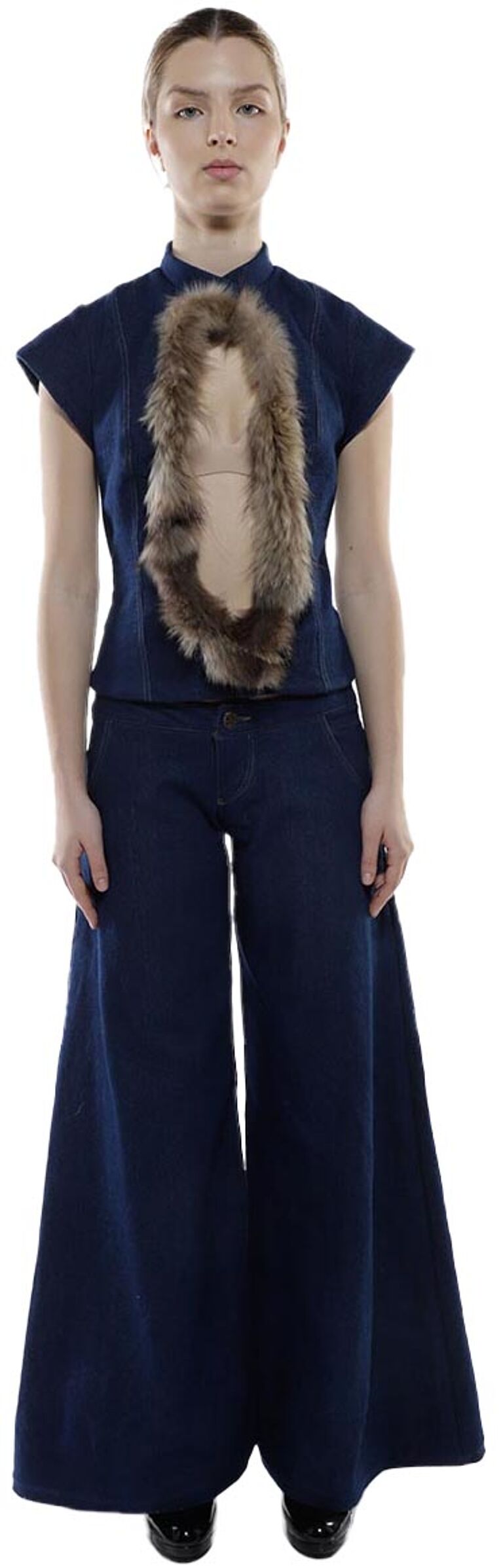 A woman with light skin and brown hair is modeling a dark blue denim jumpsuit with wide legs and a fur collar.