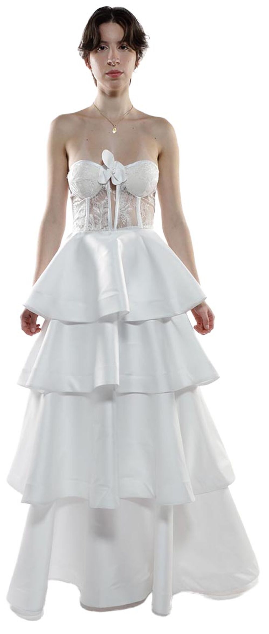 A young woman with short brown hair wears a white layered gown with a lace corset top and a delicate bow.