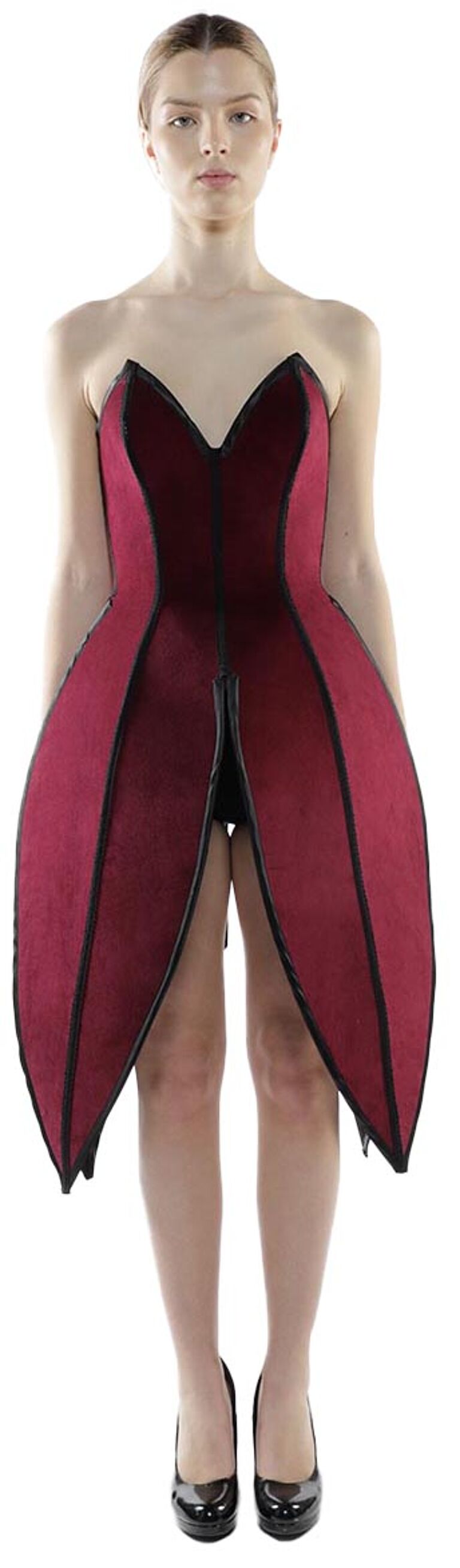 A woman with fair skin and light brown hair pulled back wears a strapless, crimson, petal-shaped dress with black trim and black high-heeled pumps.