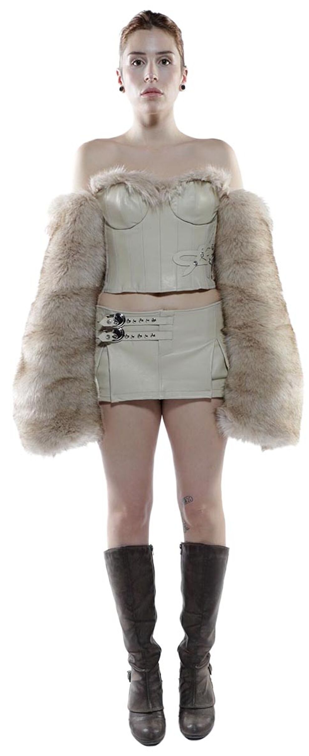 A young woman with short hair wears a cream-colored faux fur stole, corset, and mini skirt, and tall brown boots.