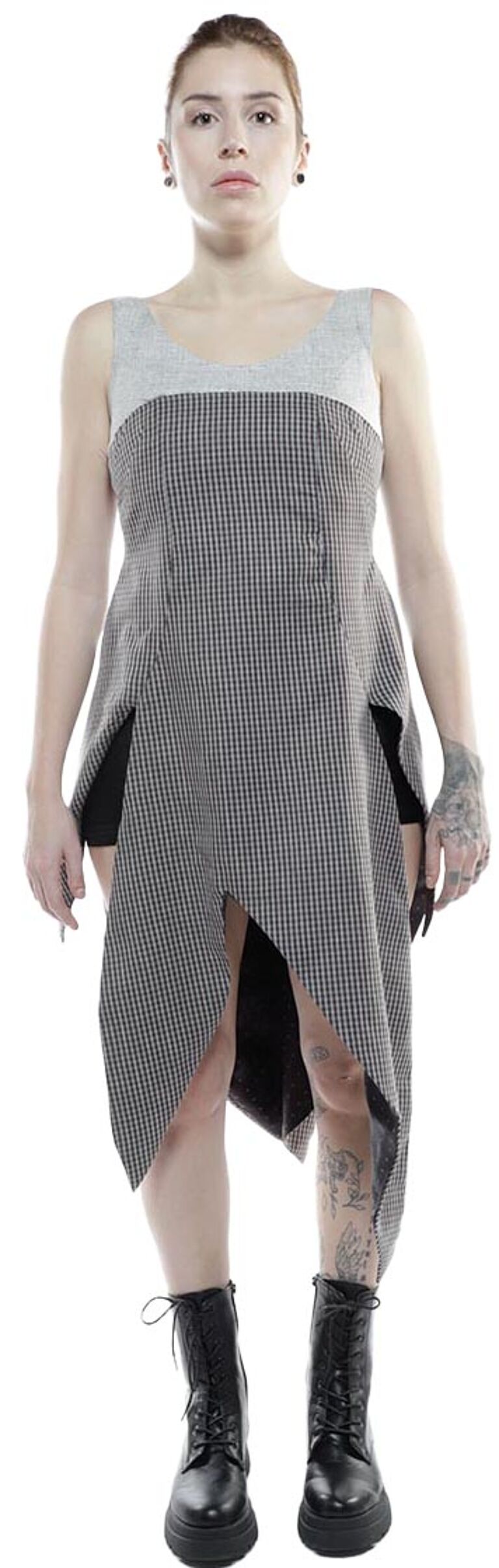 A woman with short hair and tattoos models a gray and black asymmetrical tunic dress with black boots.