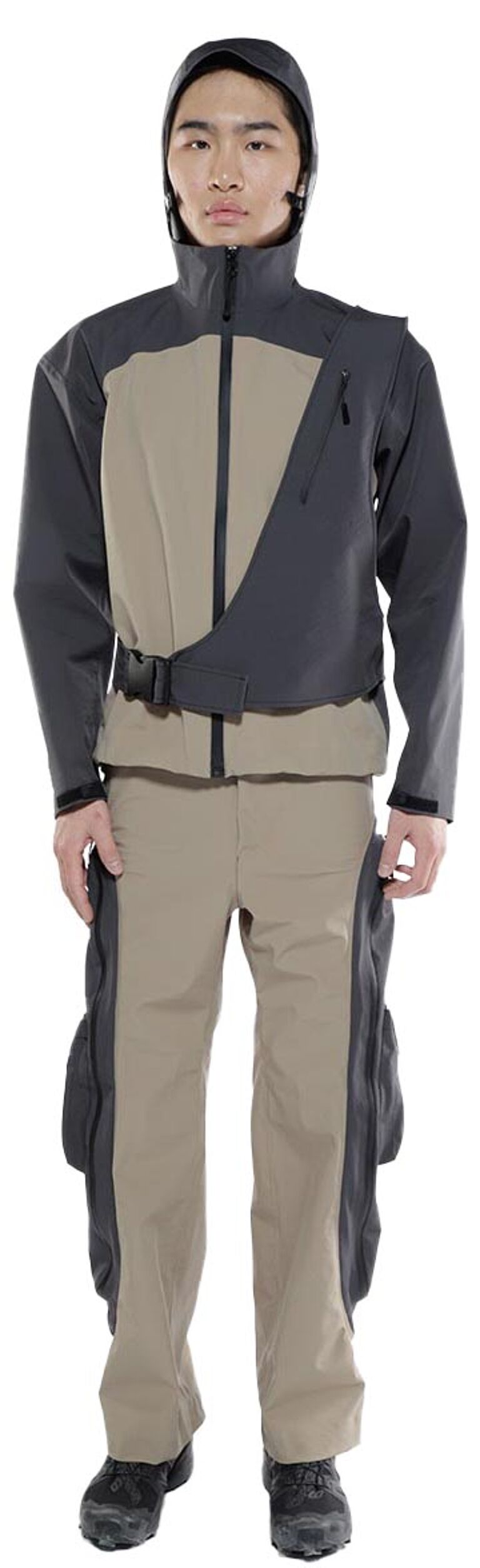 A person wearing a two-toned jacket and pants with a hood stands against a white background.
